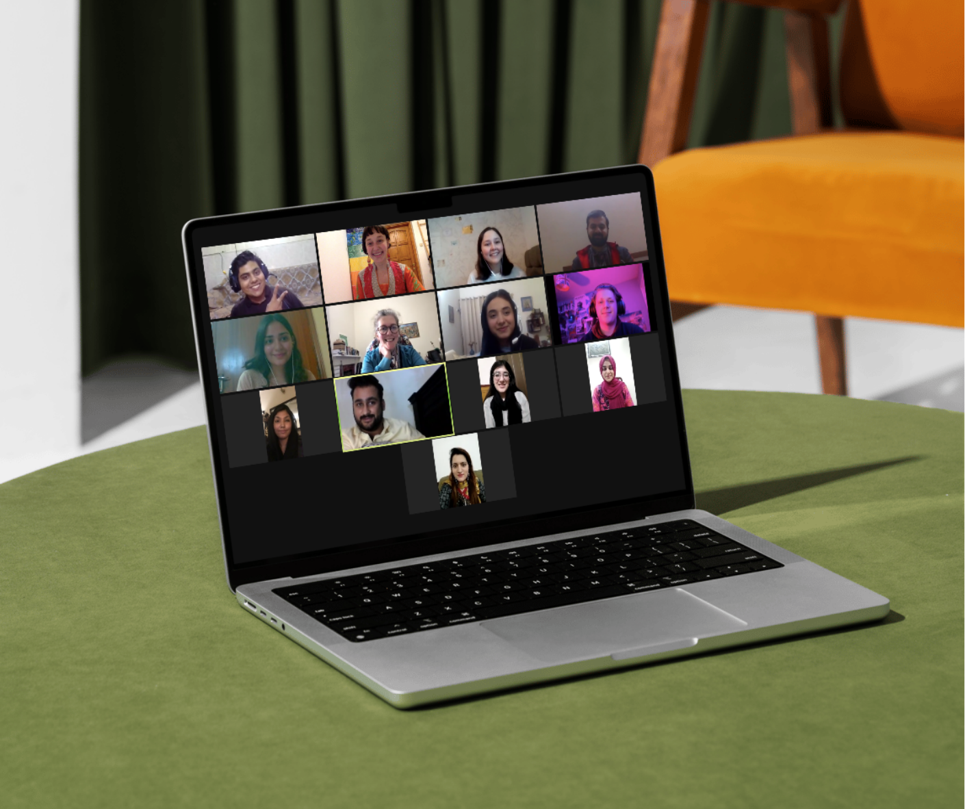Laptop on green table displaying a virtual meeting with 12 diverse participants in a grid view.