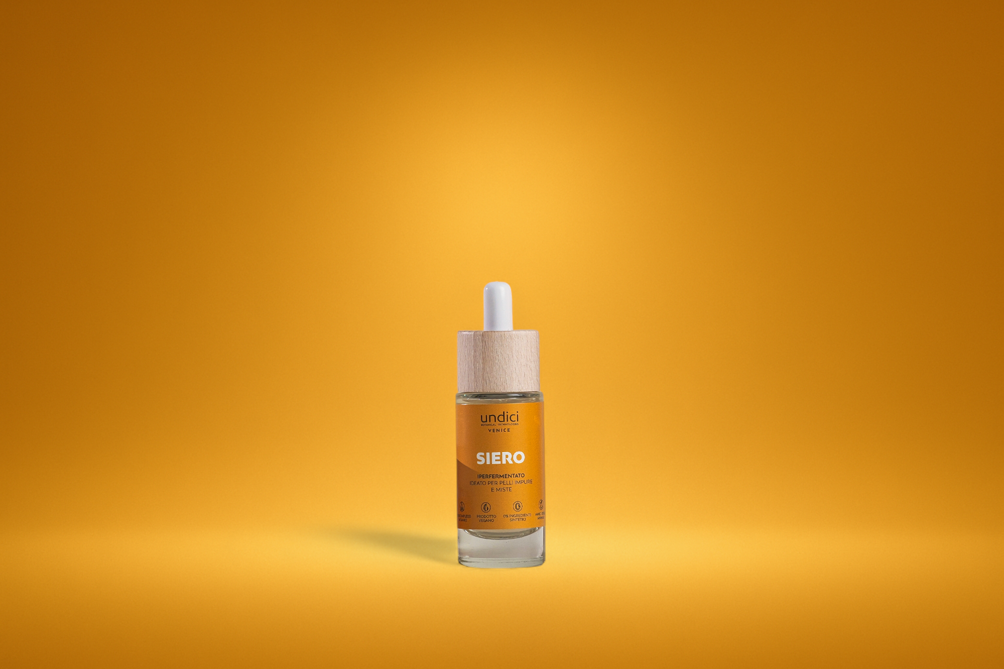 Flacone di siero con etichetta arancione e tappo in legno su sfondo giallo.