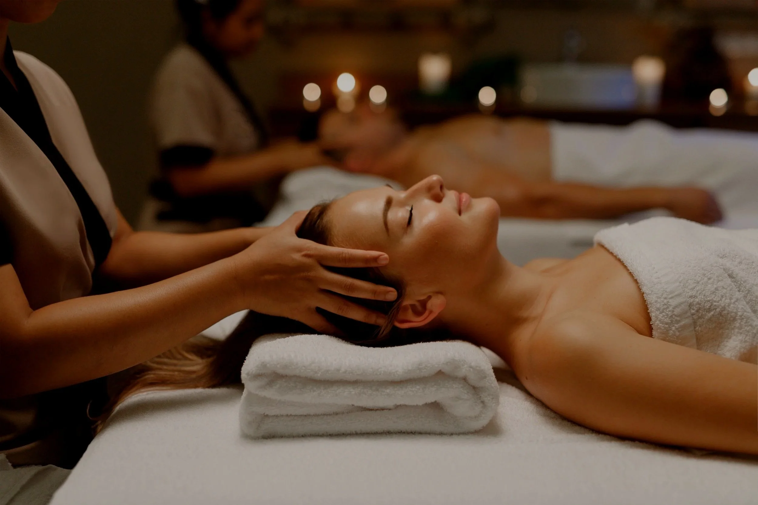 Donna che riceve un massaggio in una spa, con un'illuminazione soffusa e candele sullo sfondo.