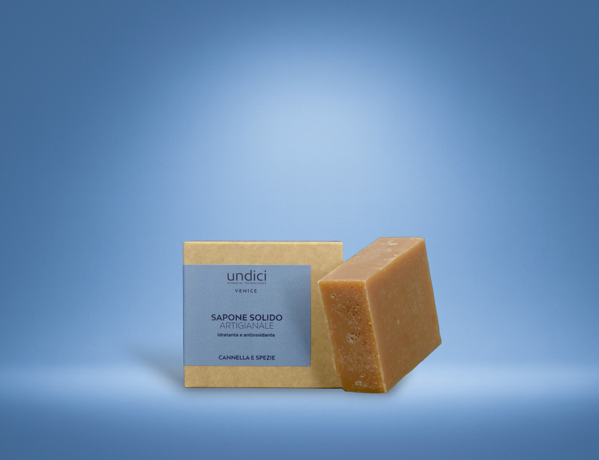 Un pacco di sapone solido artigianale con etichetta blu e una barretta di sapone accanto, entrambi su sfondo blu