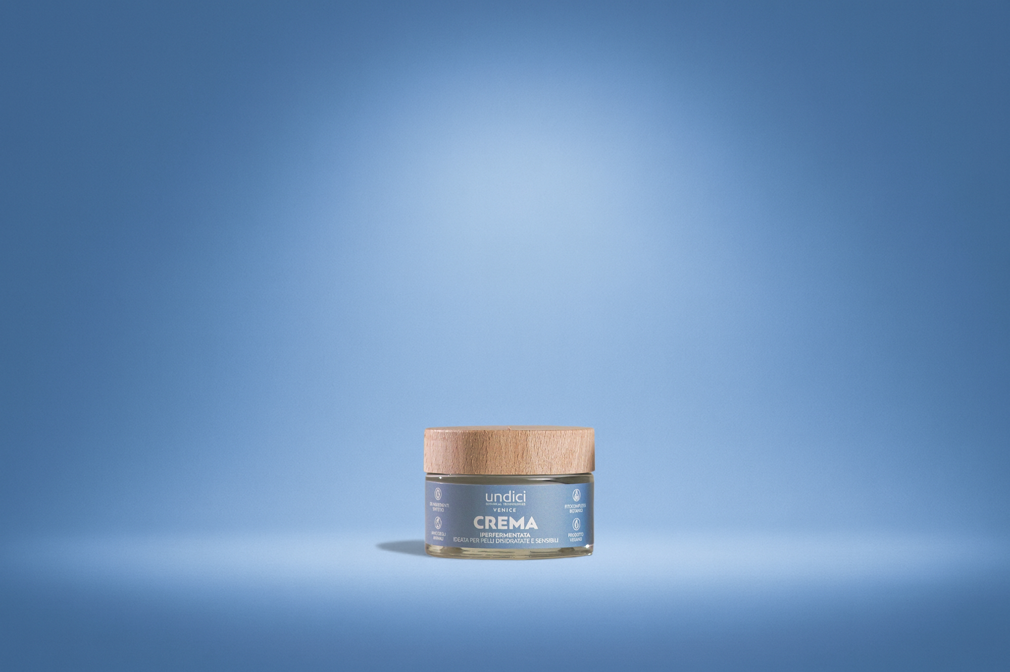 Contenitore di crema idratante con etichetta blu e tappo di legno, sfondo celeste uniforme.