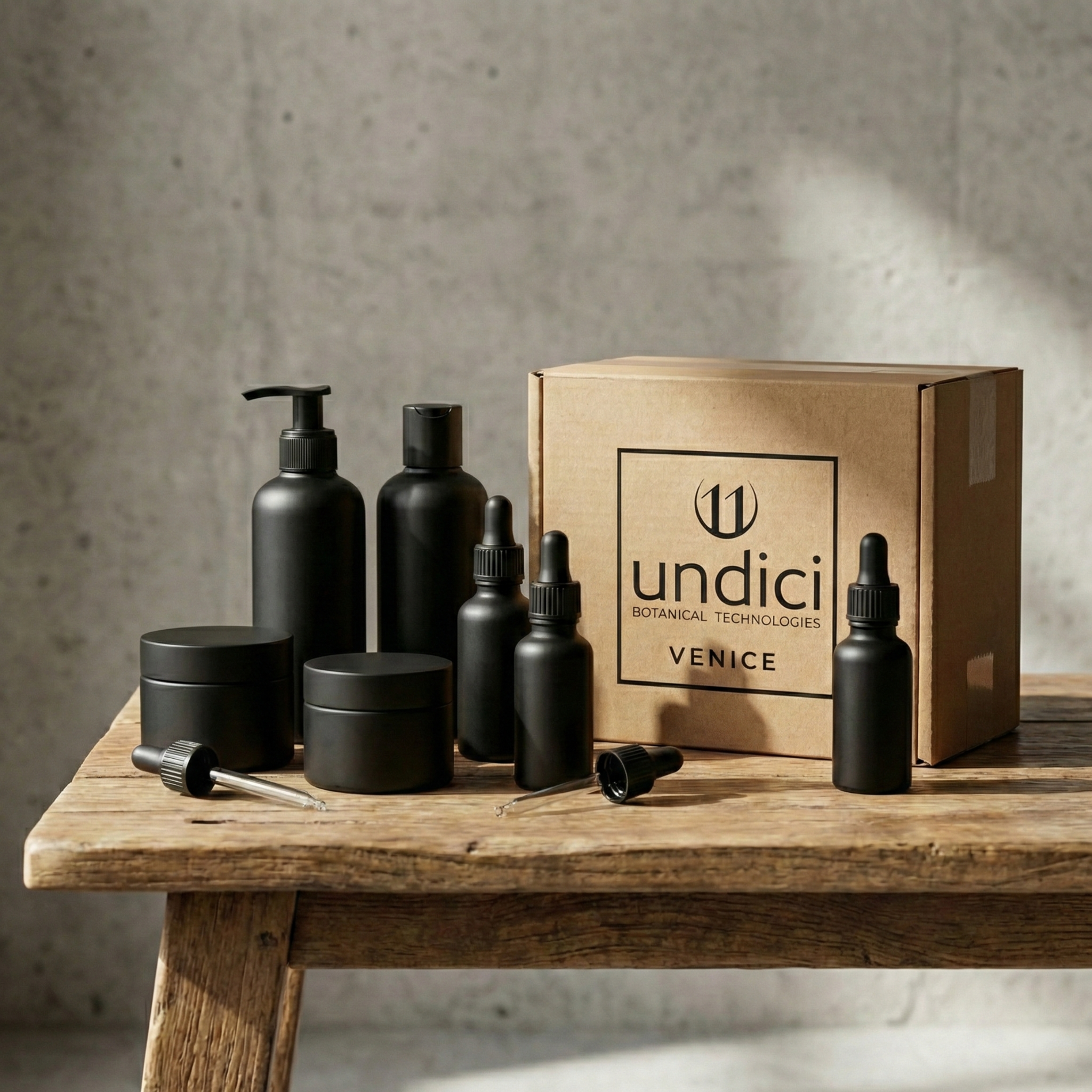 Set di prodotti cosmetici neri con pipette e dispenser su tavolo di legno, con scatola di cartone con etichetta 'Undici Botanical Technologies Venice'.
