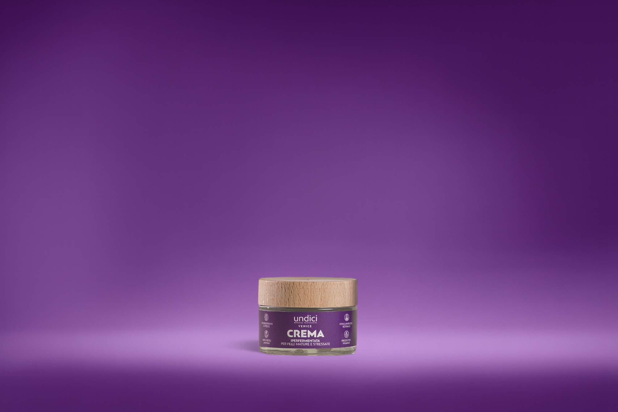 Piccolo contenitore di crema con etichetta viola e tappo di legno, sfondo viola sfumato.