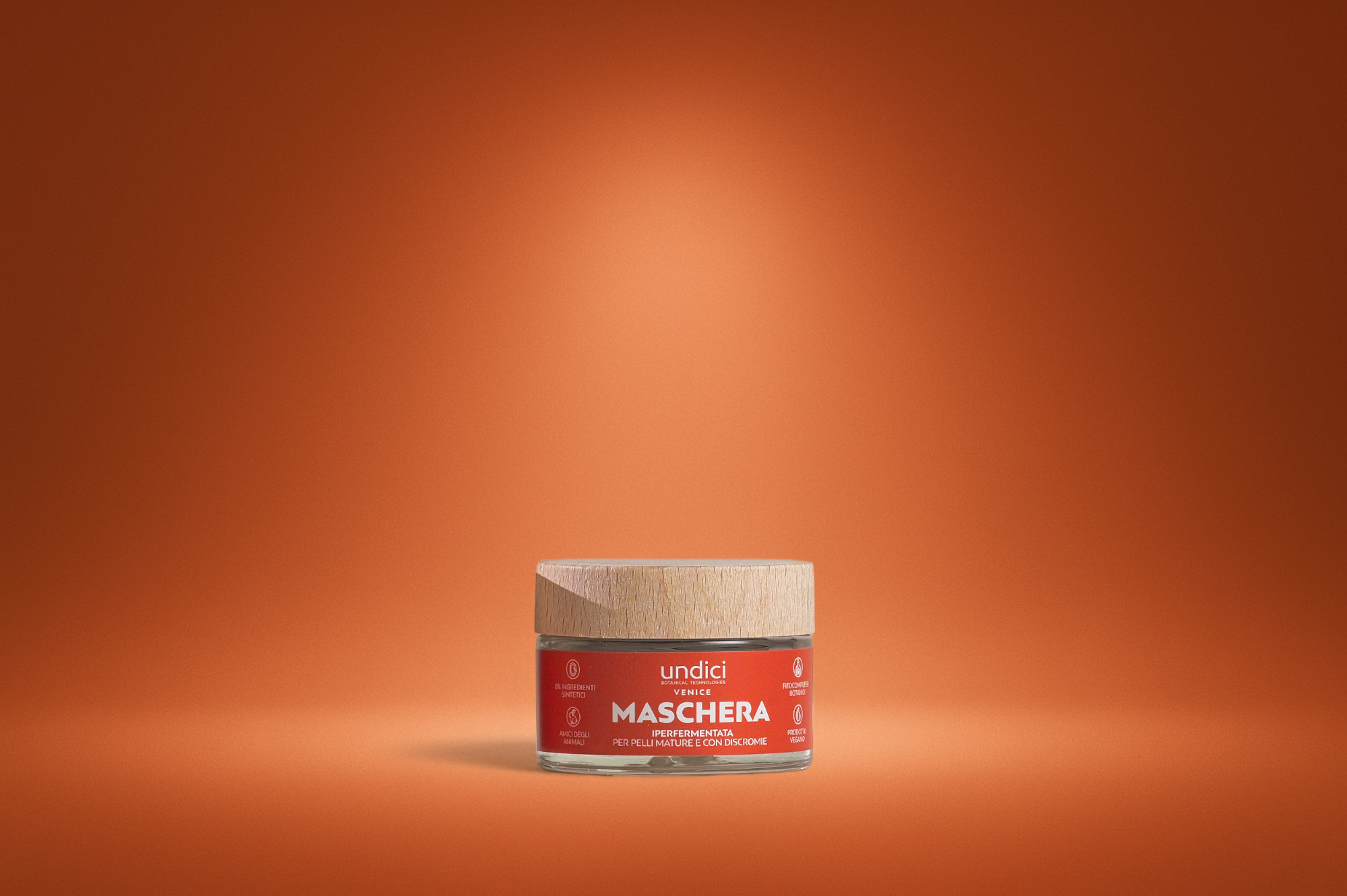 Contenitore in vetro di una maschera per pelli mature e con discromie con etichetta rossa, sullo sfondo arancione