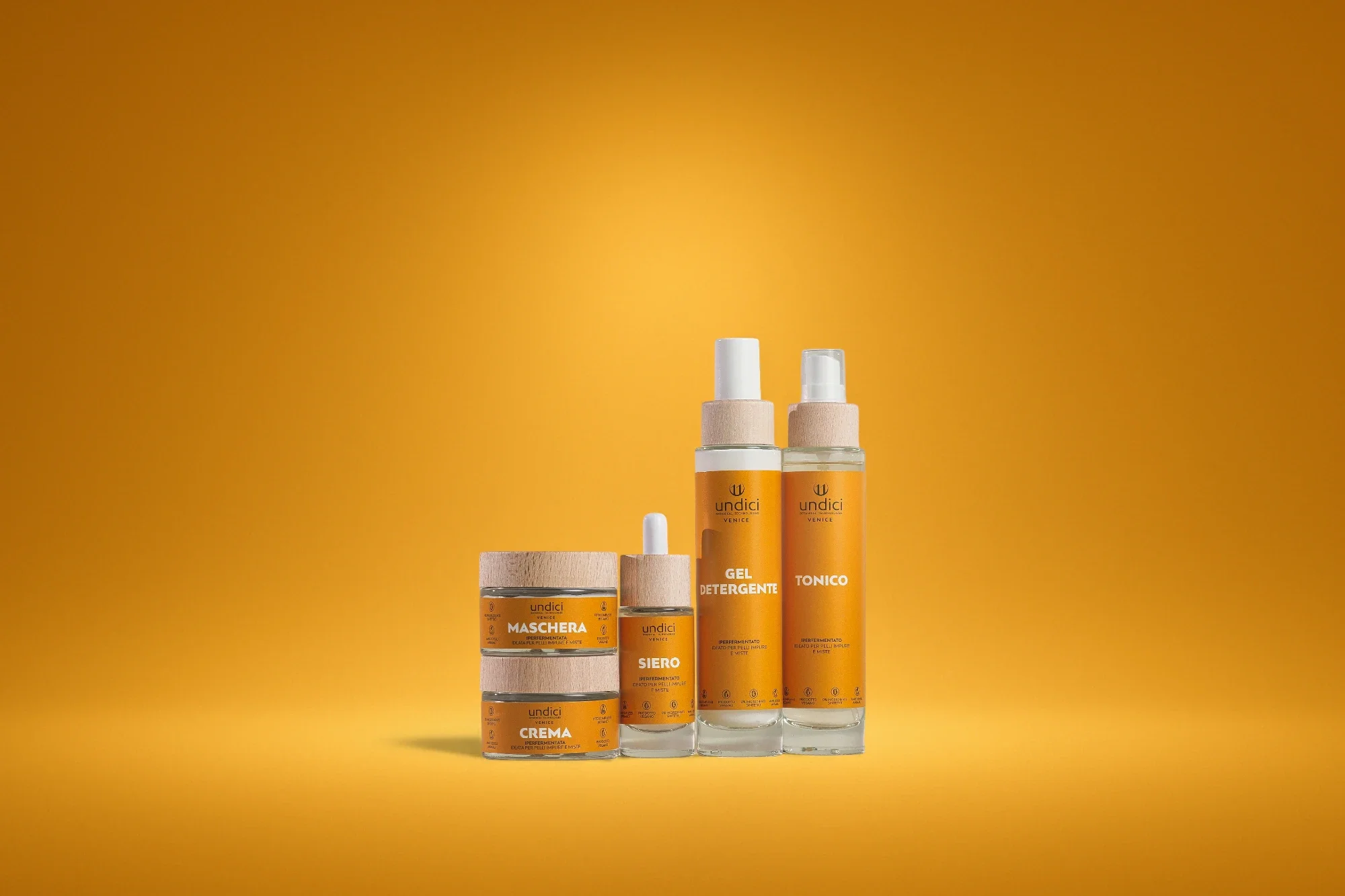 Set di prodotti per la cura della pelle, tra cui crema, siero, gel detergente e tonico, con etichette arancioni, su sfondo giallo