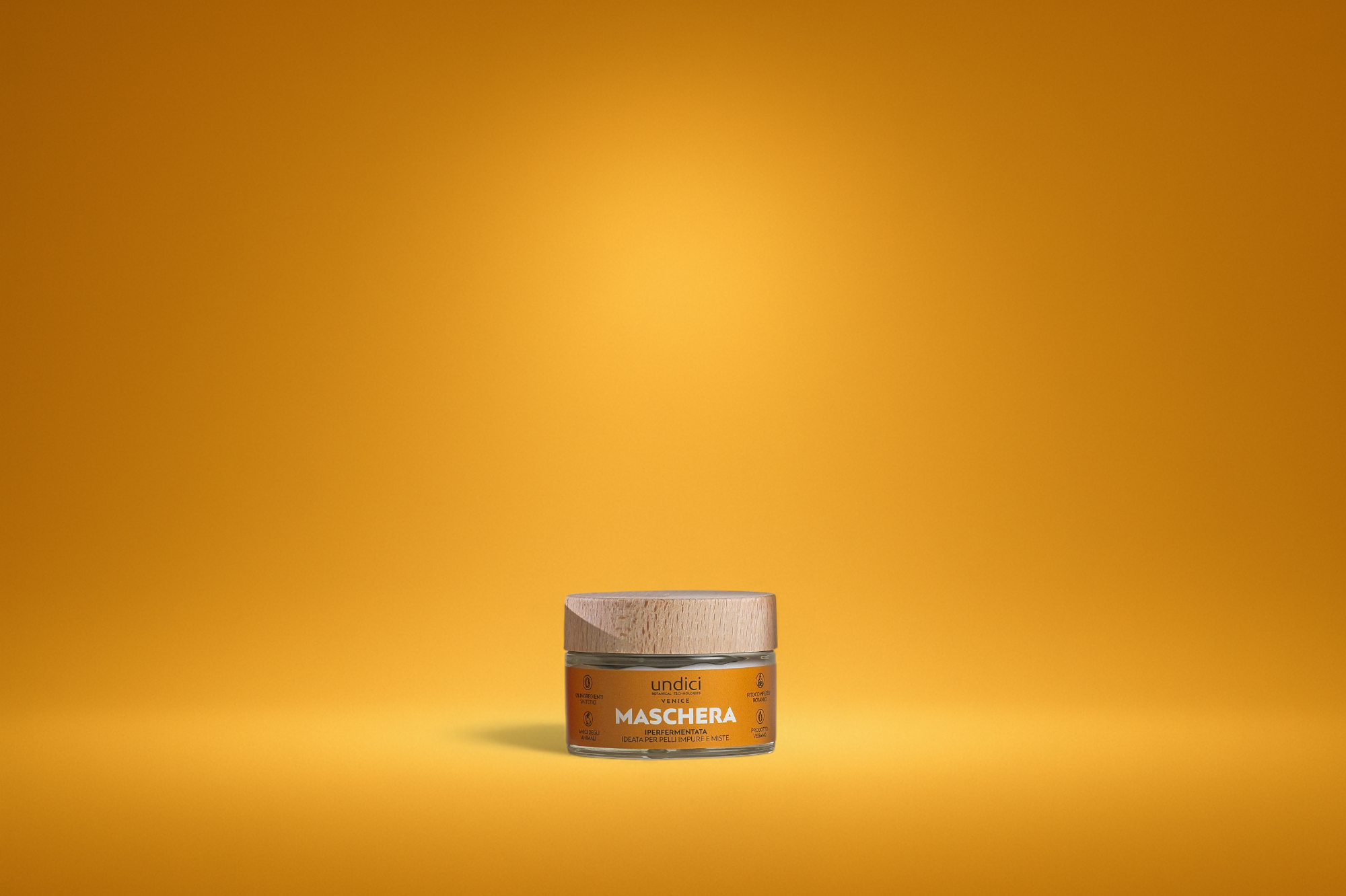 Contenitore di crema facializzata con etichetta arancione e tappo di legno, posizionato su sfondo giallo