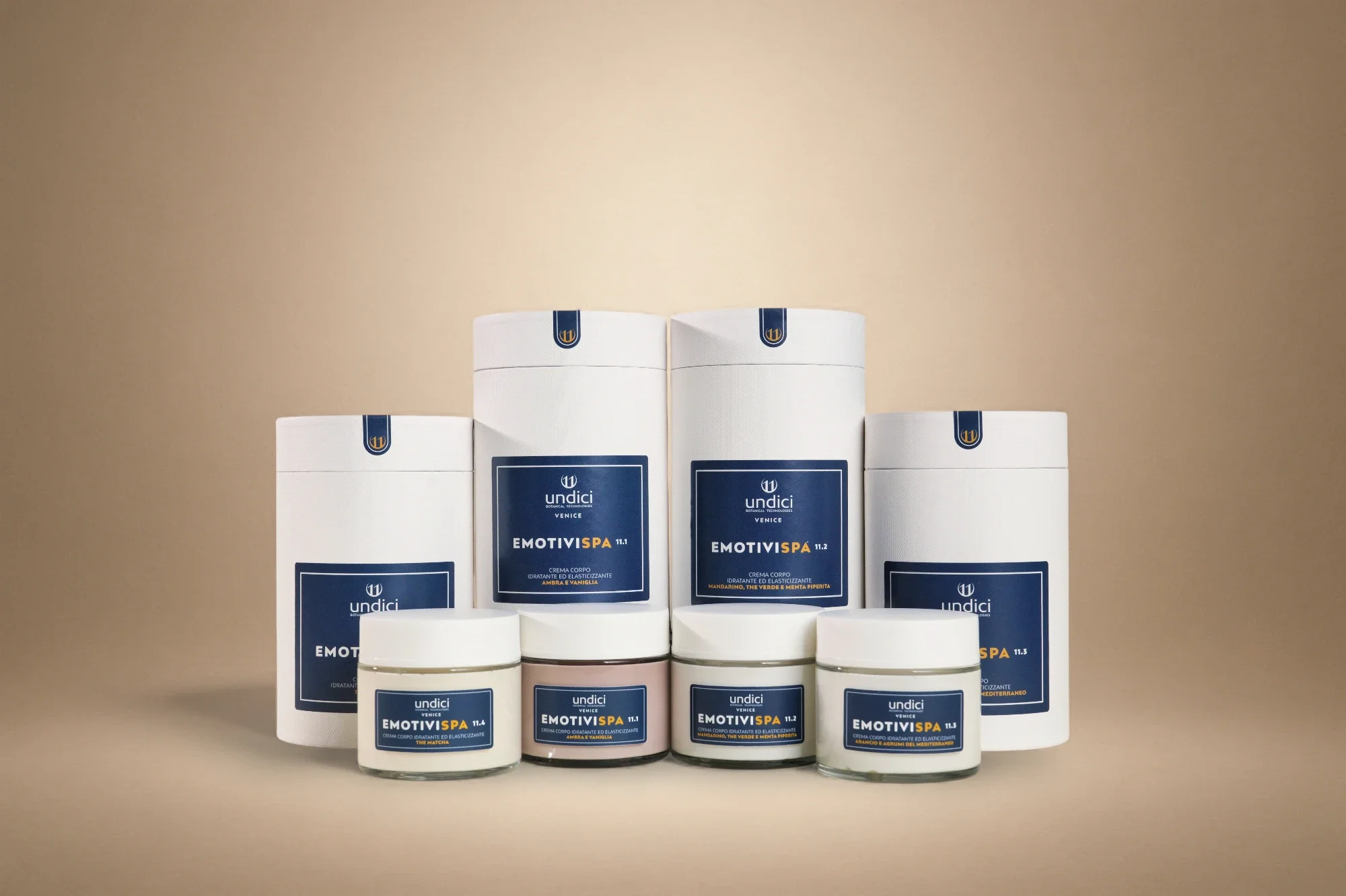 Diversi tubetti e barattoli di prodotti per la cura del corpo con etichette blu scuro e dettagli arancioni su sfondo beige.