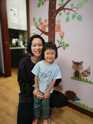 A woman and a girl smiling and posing in front of a colorful wall mural with animal illustrations and a height chart.