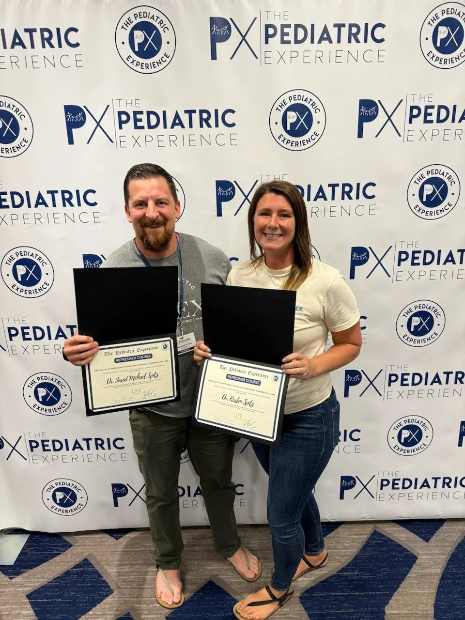 Dr Jared and Dr Kirsten holding their "The Pediatric Experience" Certificates while smiling displaying professional merit for pediatric chiropractic care.