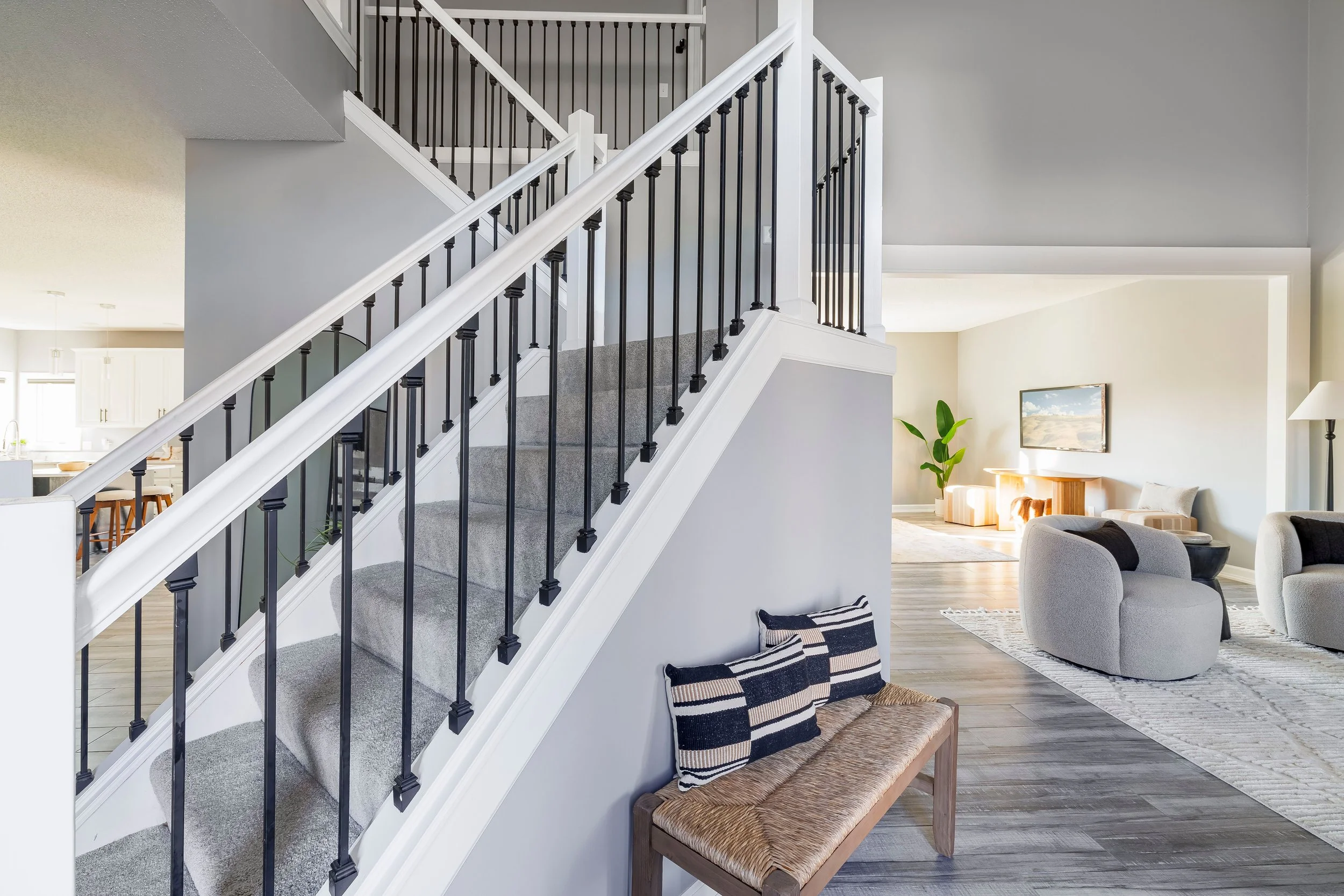 Living room with staircase, gray walls, and modern furniture including a gray chair, a side table, and a large rug.