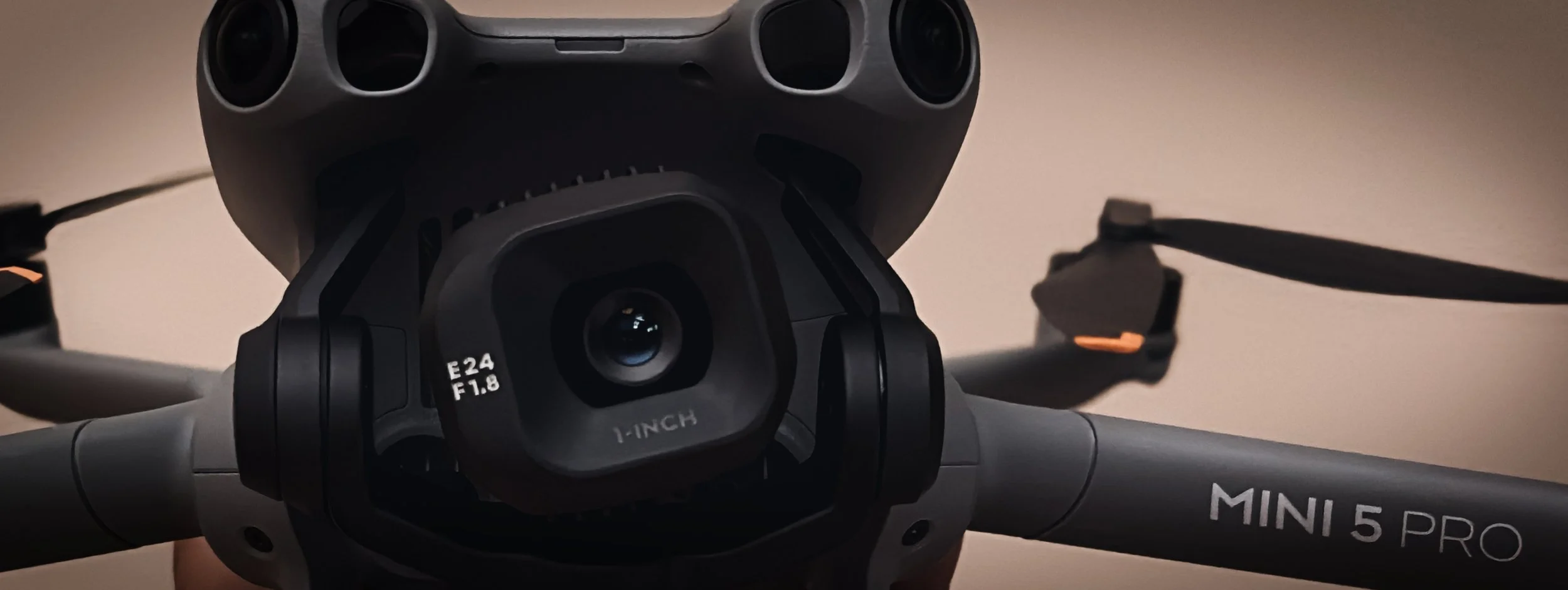 Close-up of a DJI Mini 5 Pro drone with a camera lens and gimbal, showing part of the drone's body and propellers.