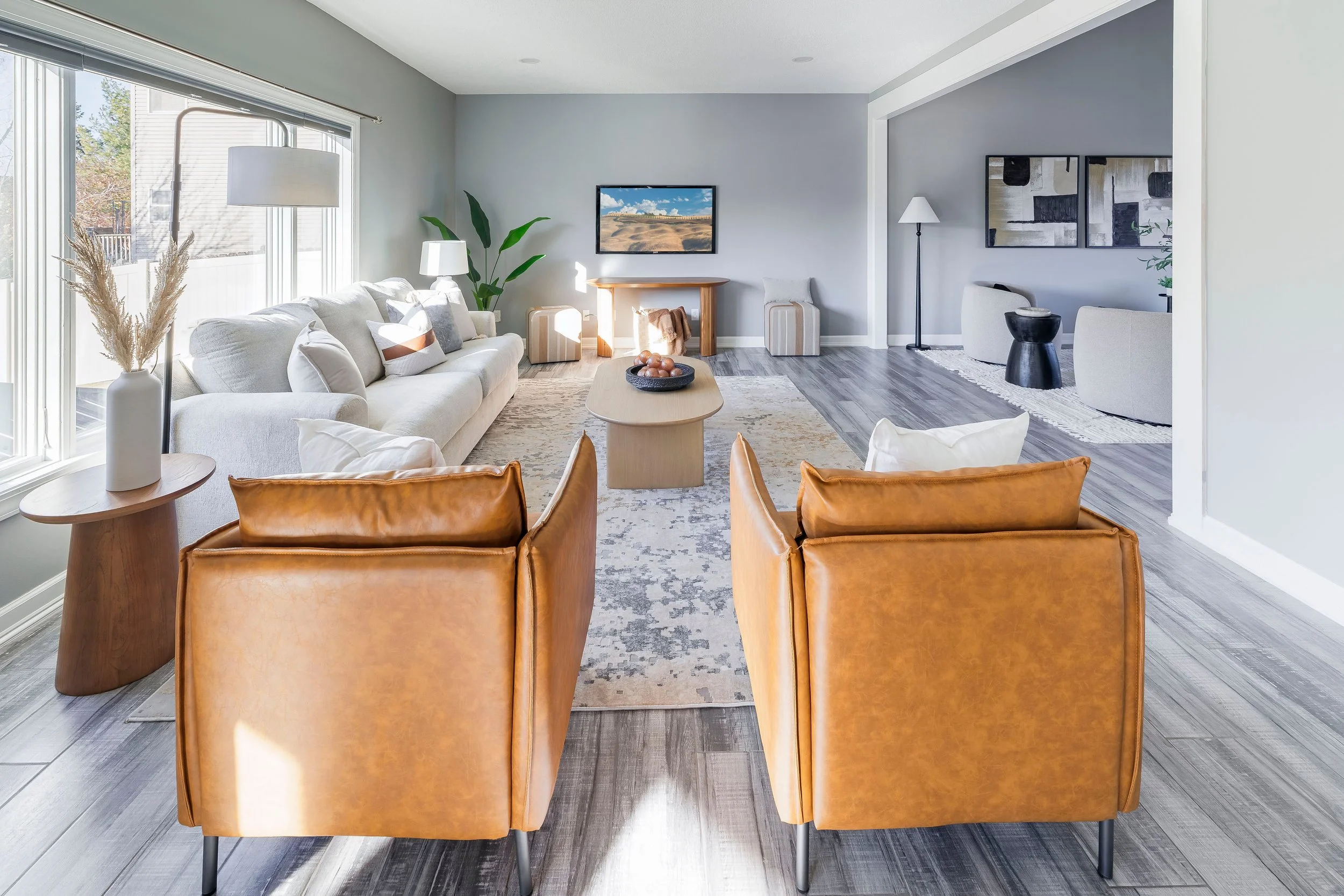 Living room with beige sofa, two caramel leather armchairs, and a view of a gray wall, wooden floor, coffee table, and various modern decorative elements.