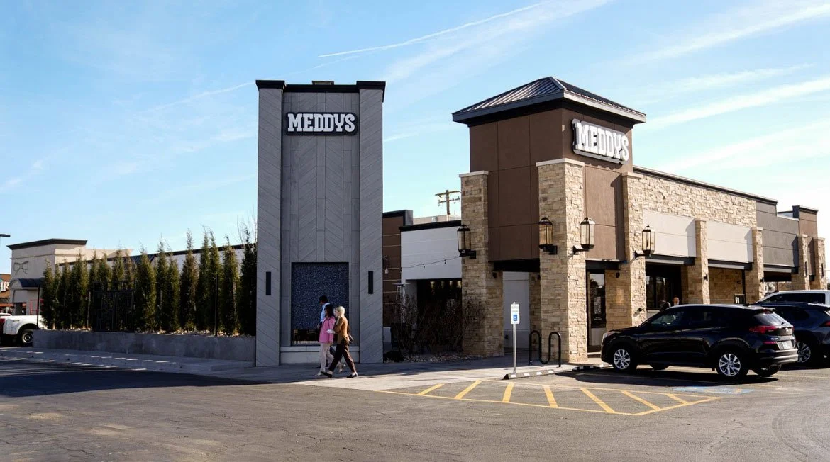 Meddys restaurant exterior with parking lot, people walking, and a clear sky.