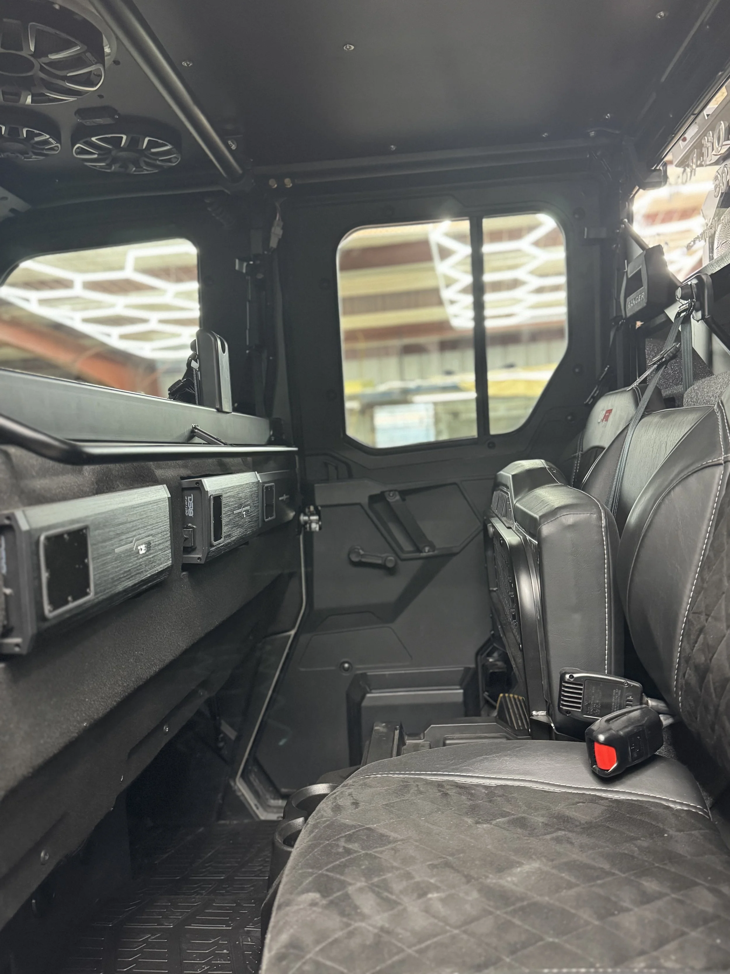Interior of a rugged vehicle with black seats, dashboard, and windows showing a glimpse of a warehouse or garage.