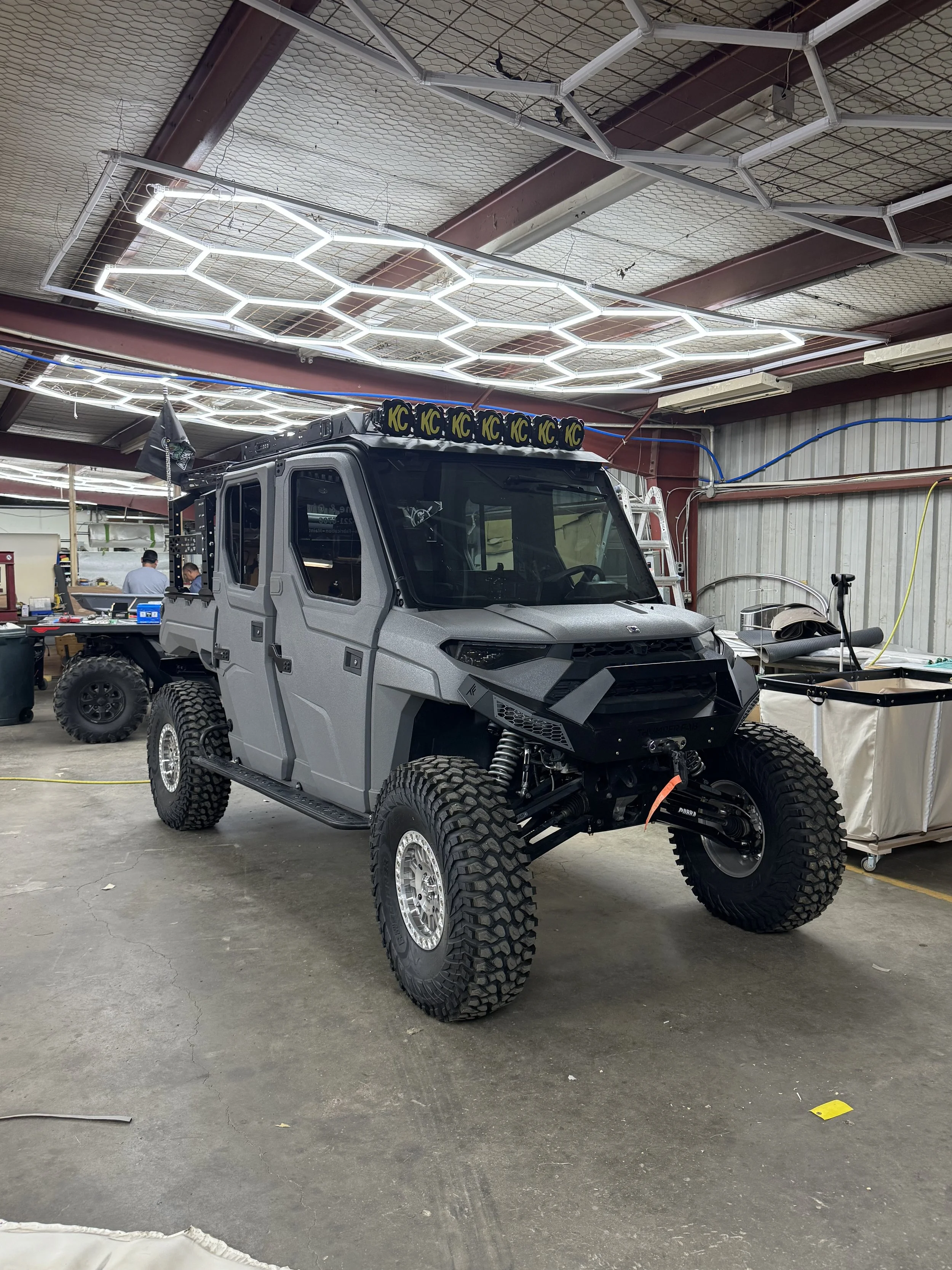 Gray off-road utility vehicle with large tires and a rugged design inside a workshop.