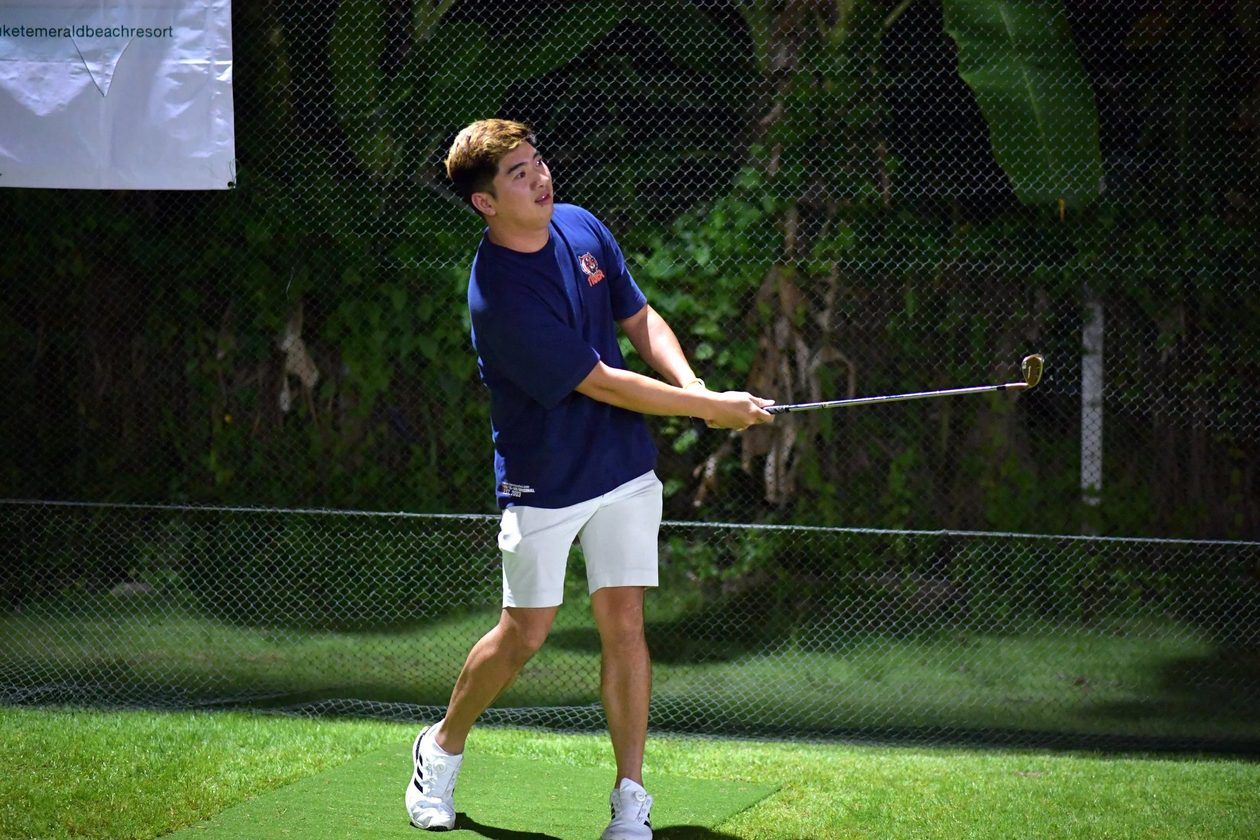 Young man playing golf on a night-lit course, swinging a golf club.
