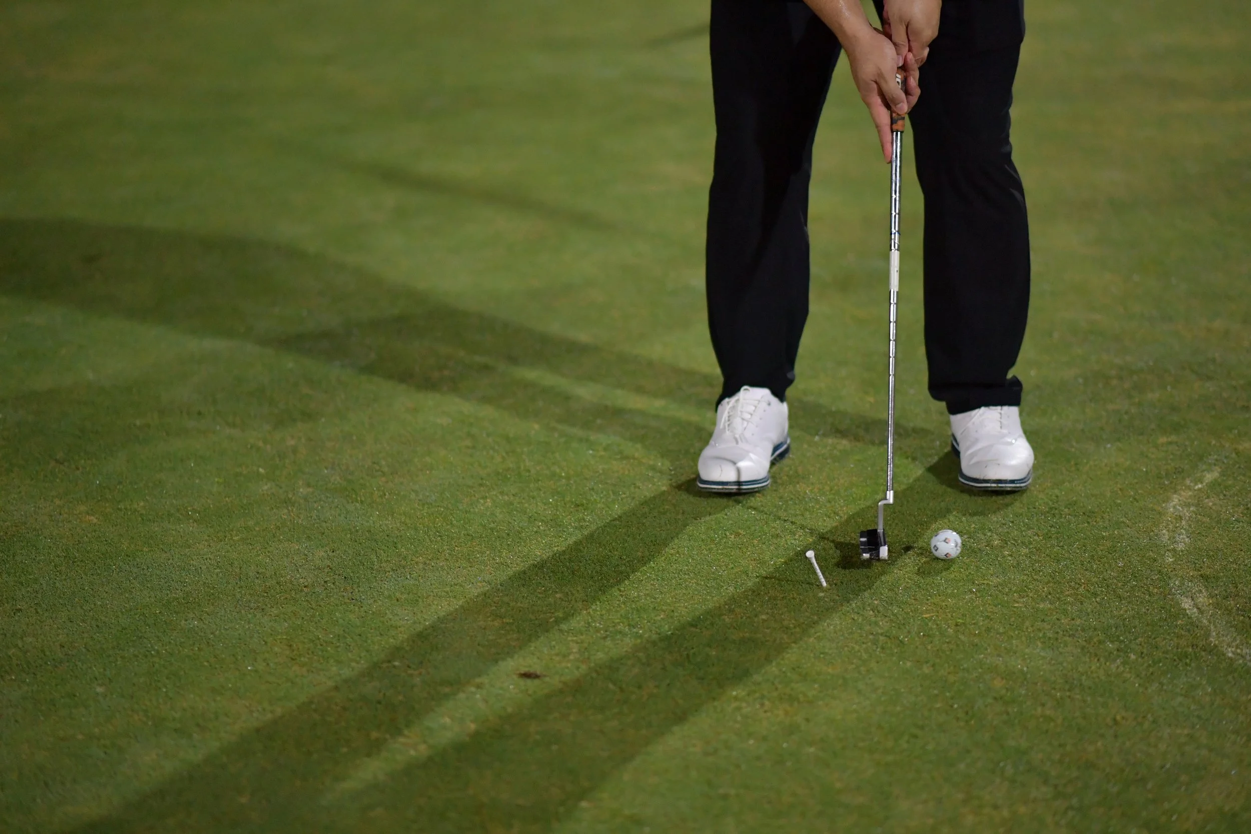Person on a golf course preparing to putt with a golf club, golf ball, and tee on the green grass.