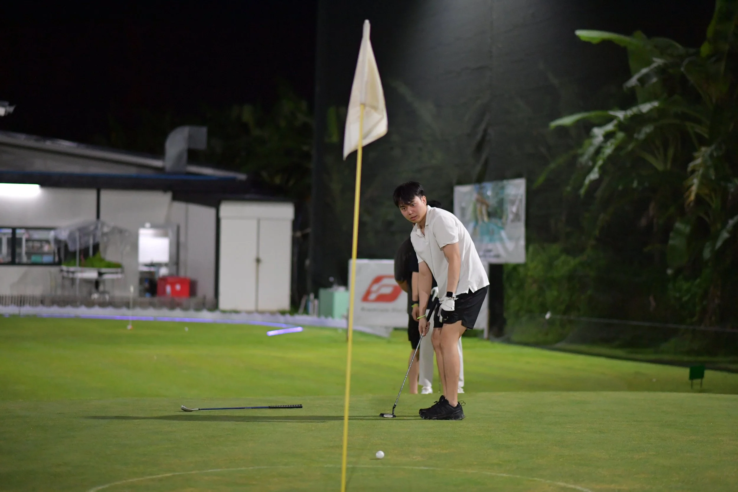 Young man playing golf at night on a golf course, preparing to putt the ball near the hole.