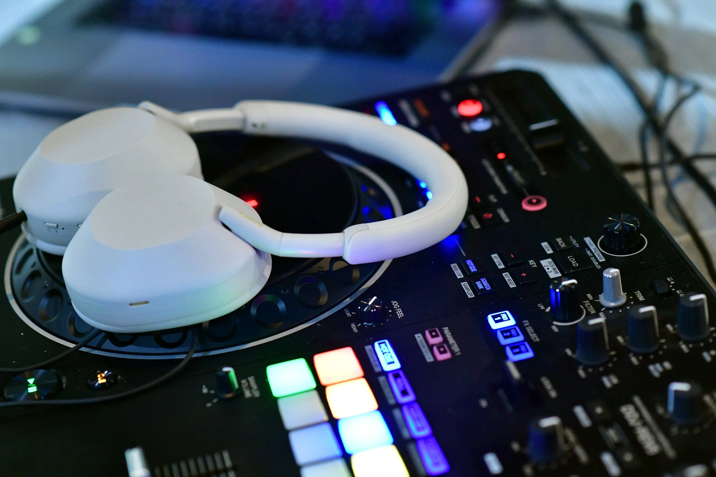 White over-ear headphones placed on a DJ controller with colorful LED lights.
