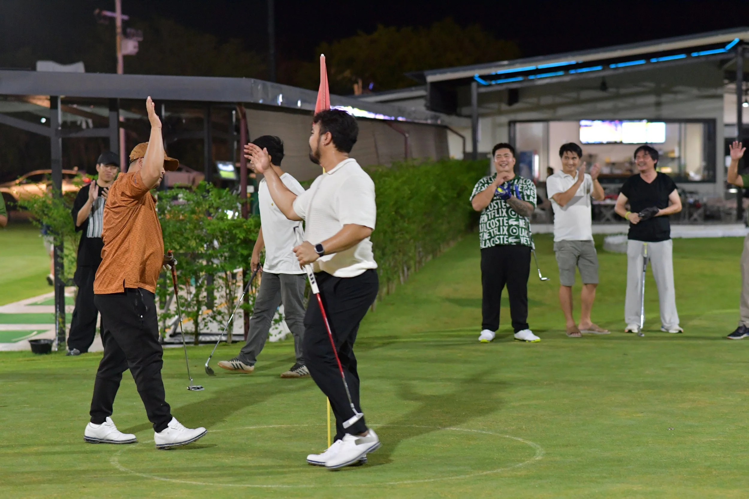 A group of people on a golf course at night, celebrating and giving high-fives after a game.