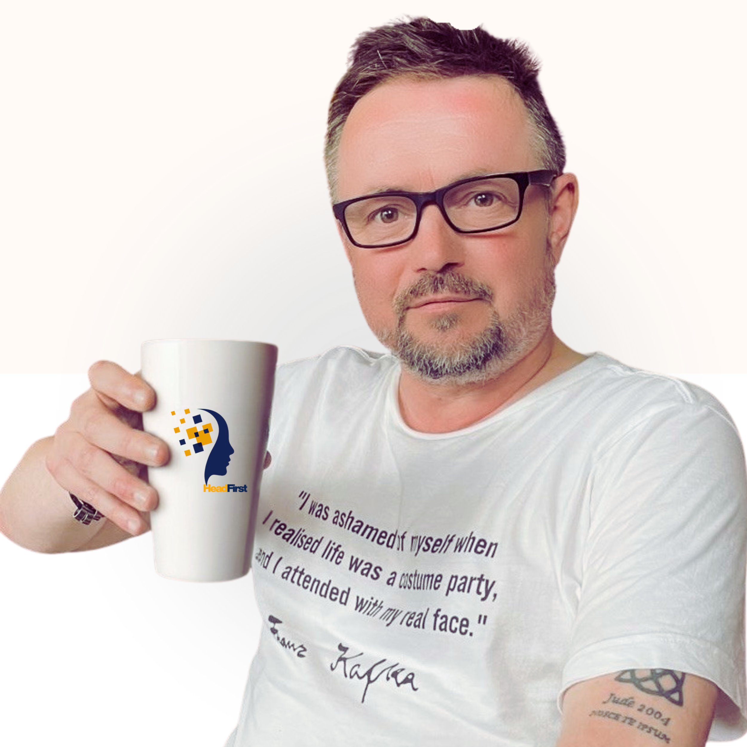 A man with glasses and a beard holding a white mug with a logo of a human face profile and the text "HeadFirst". He is wearing a white t-shirt with a quote: "I was ashamed of myself when I realized life was a costume party, and I attended with my real face."