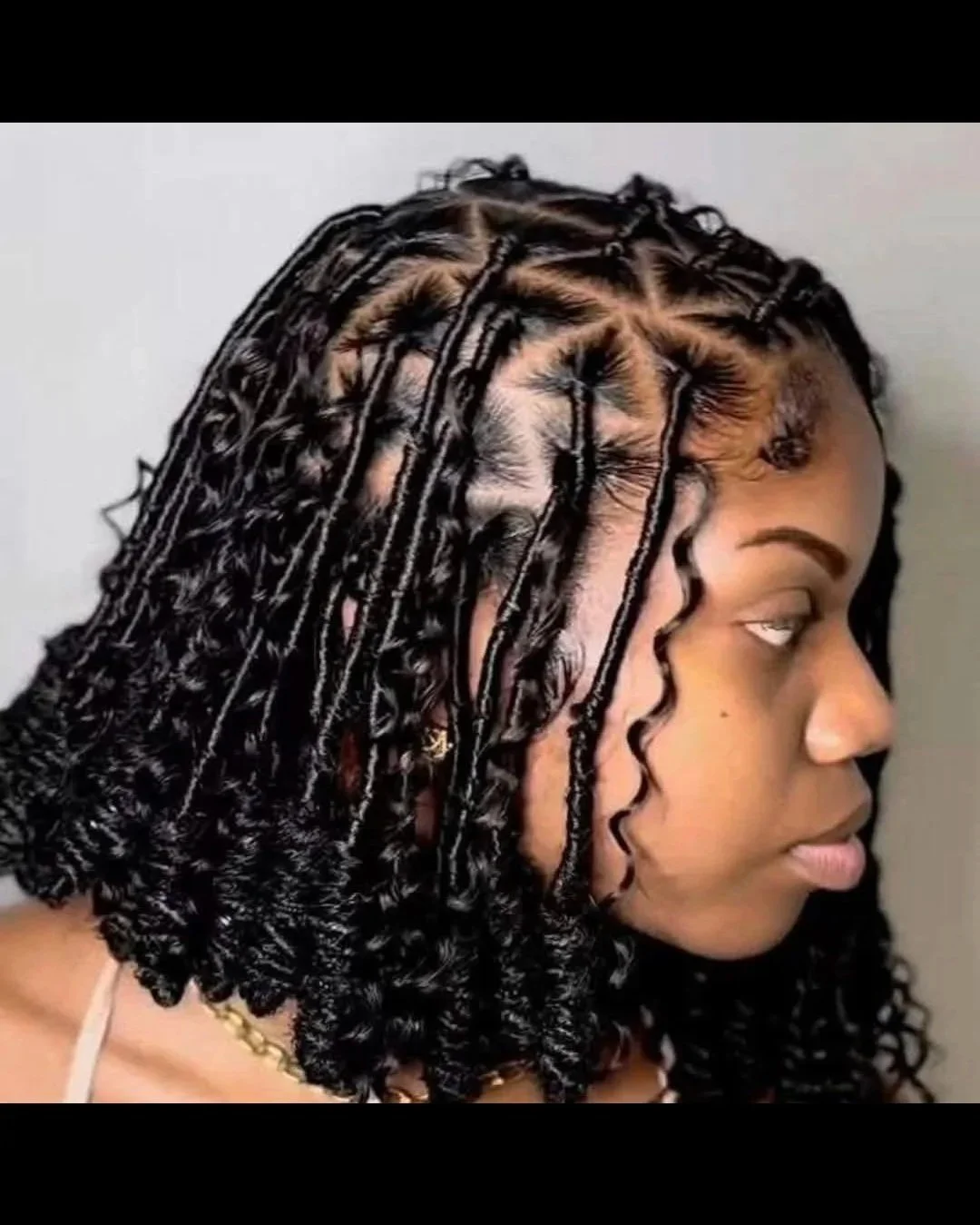 Side profile of a woman with short, curly black hair styled in twists that end in curls.
