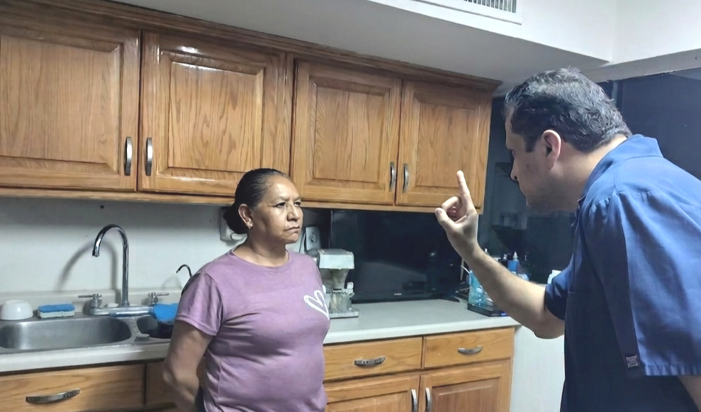 Una mujer con camiseta morada es evaluada y revisada por el Doctor Jorge Emilio García, quien usando su dedo índice como guía, ajusta la mirada de la nueva prótesis que utilizará la paciente.