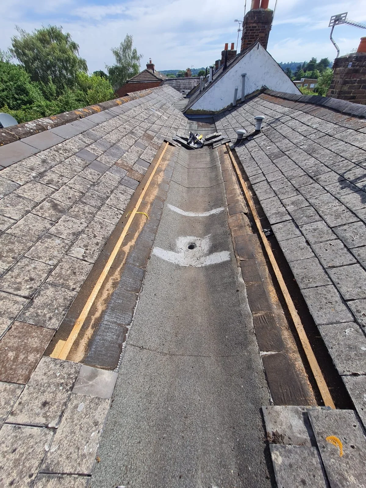 Flat roof valley repair showing felt membrane and drainage channel between two pitched roofs