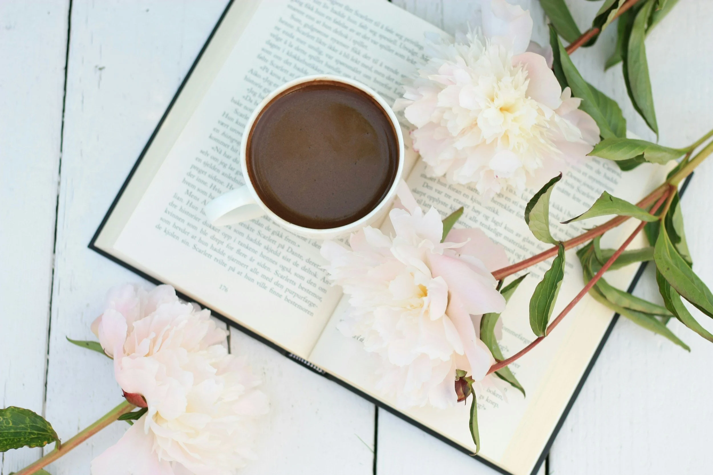 Image of an open book with a cup of coffee and flowers arrayed around it. This speaks to the idea of Soul Readings opening up to a page in someone's life and understanding the souls purpose