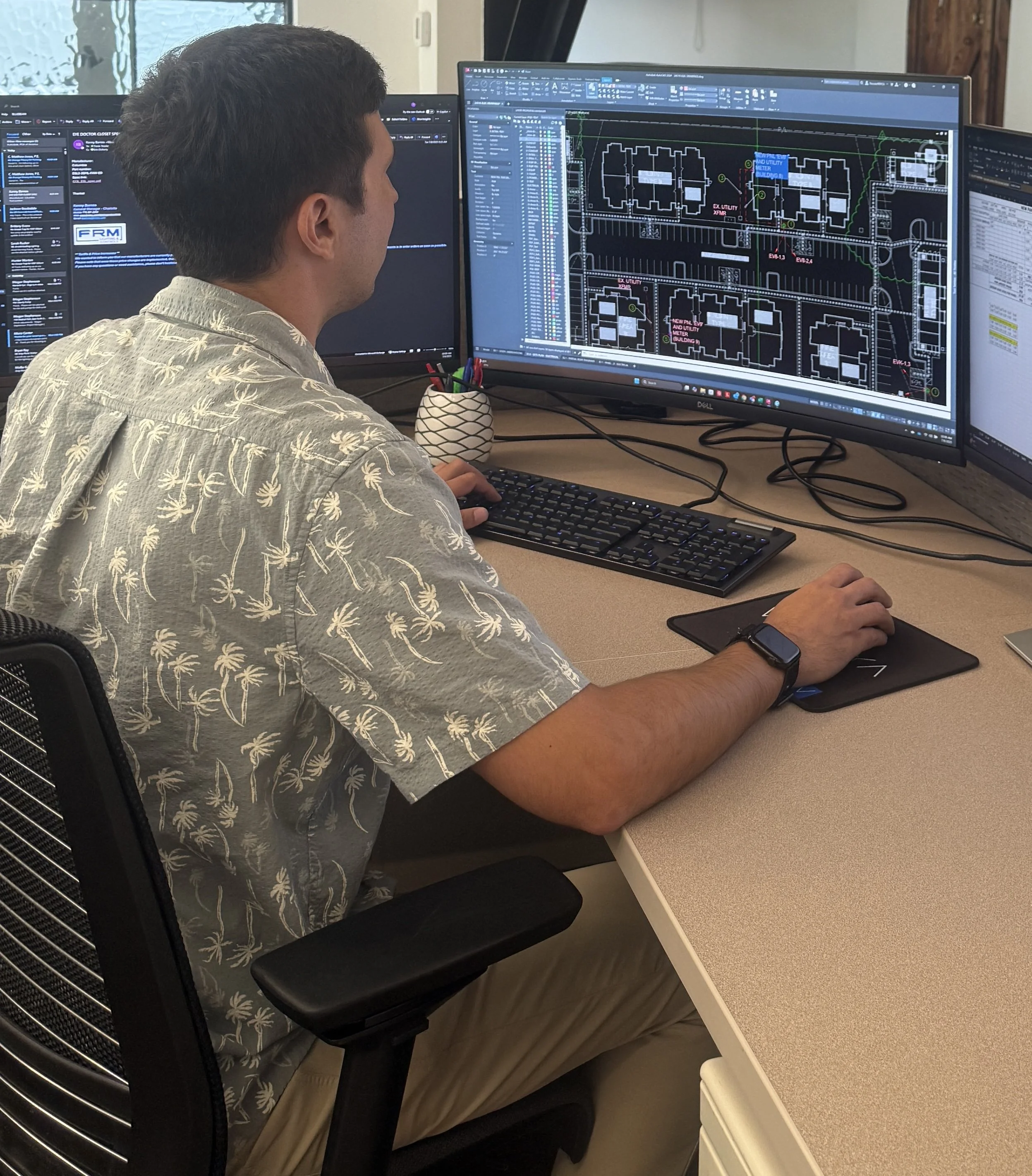 A man is working at a desk with three computer monitors displaying architectural design software and building plans.