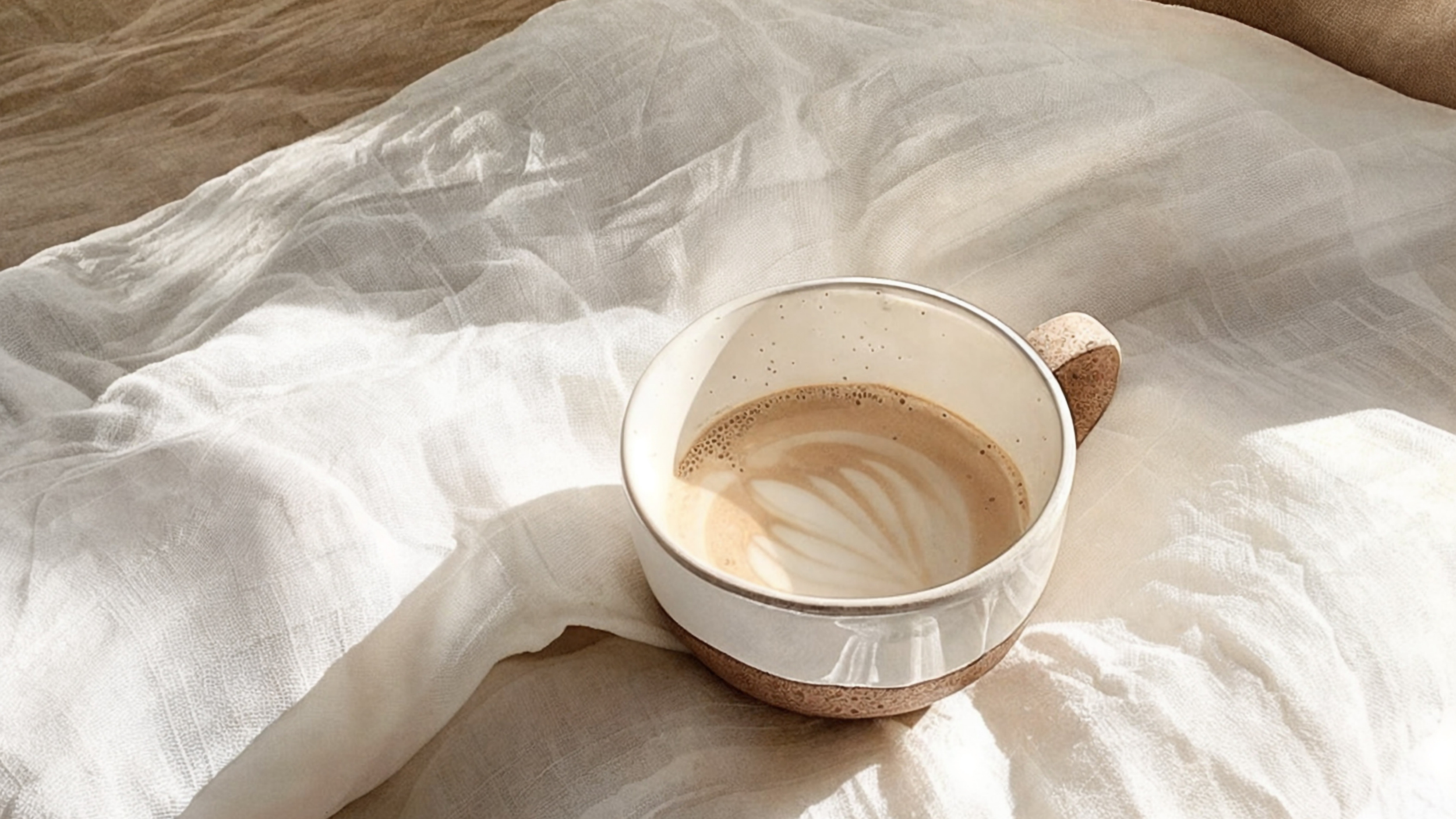 Terracotta and glazed cup filled with cappucino on white cotton sheets