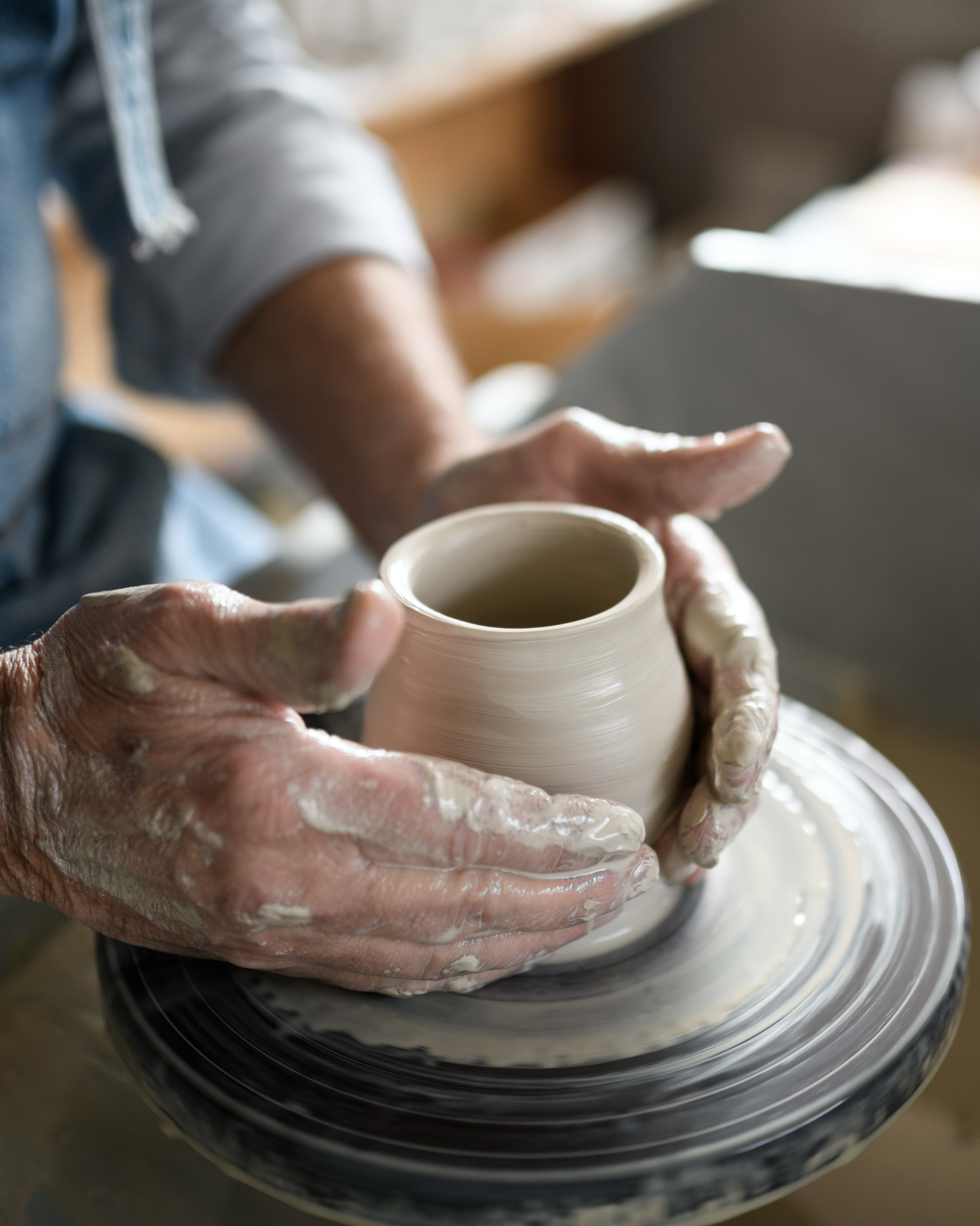Hands shaping a clay pot on a pottery wheel.