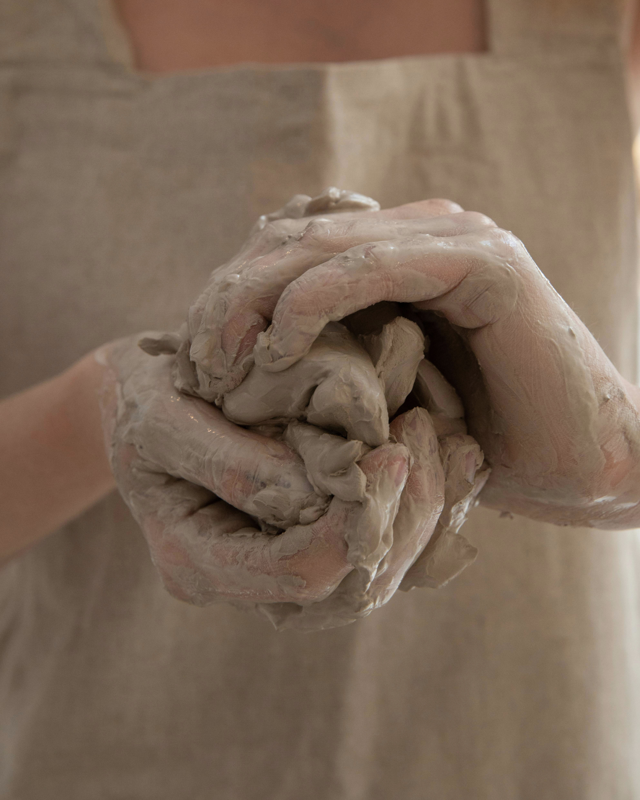 Person wearing a beige apron kneading grayish dough with hands covered in flour.