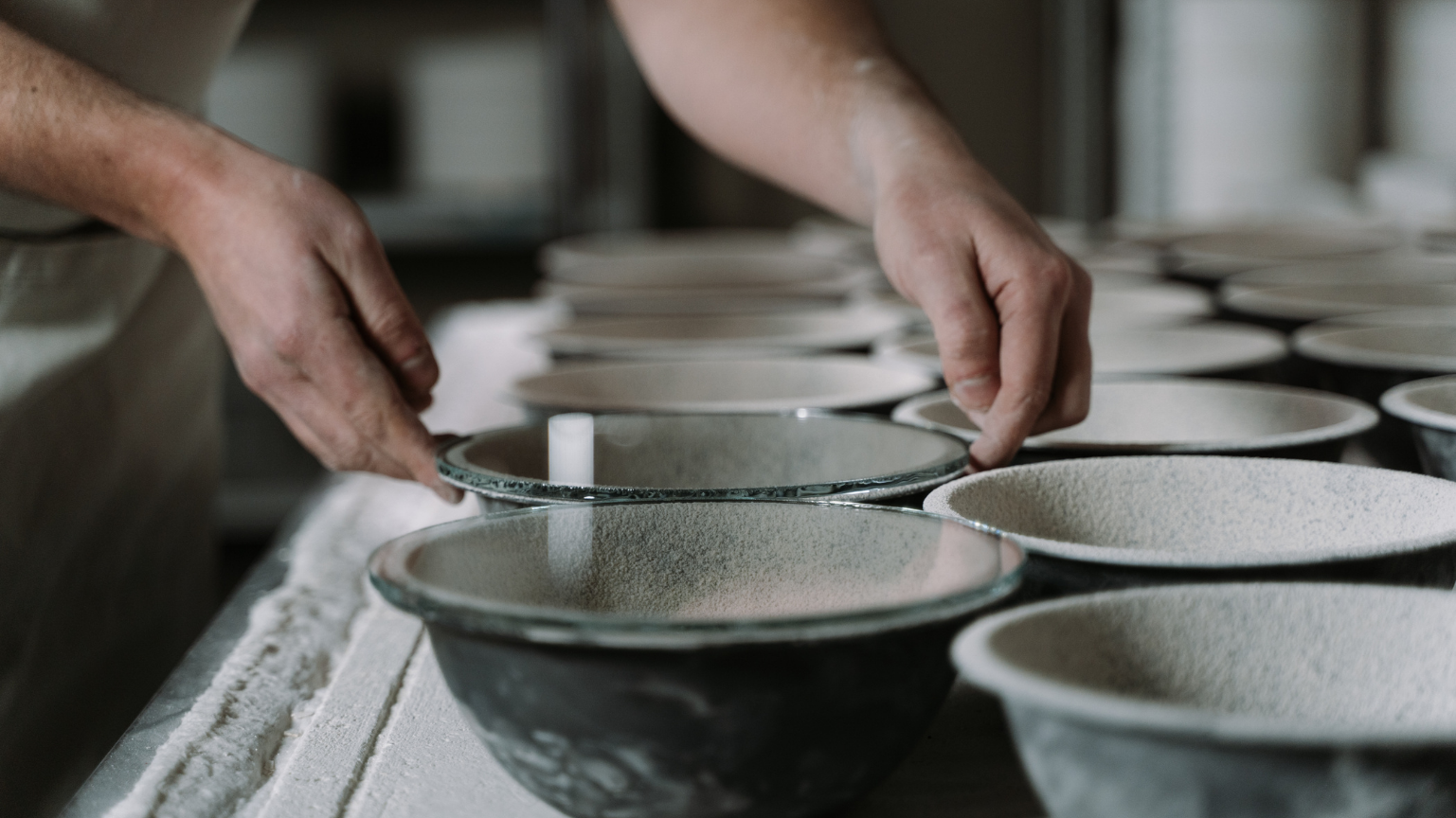 Hands working with ceramic bowls on a worktable.
