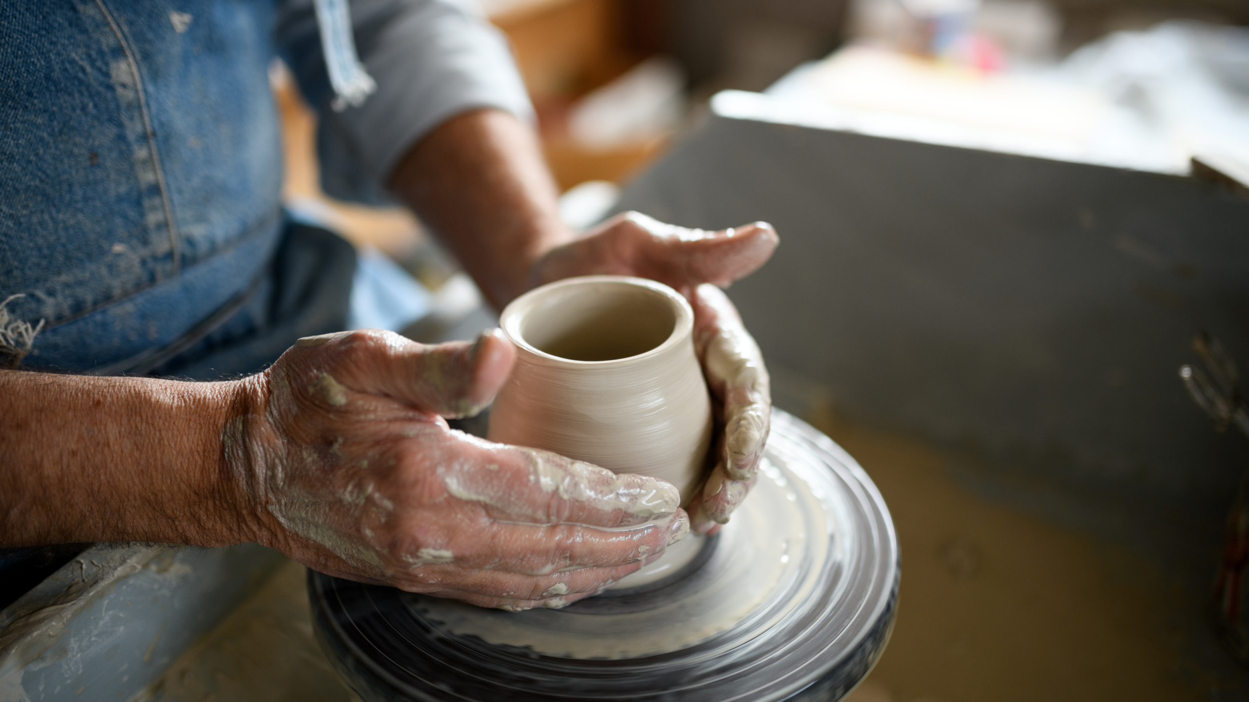 Person shaping a ceramic pot on a pottery wheel in a workshop.
