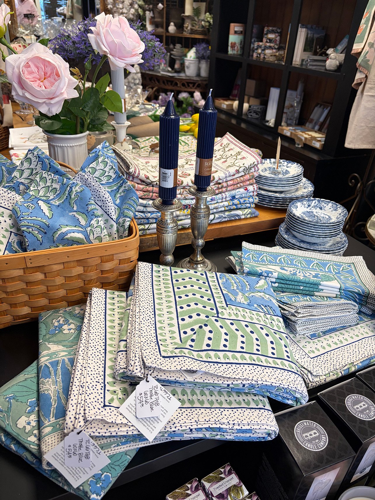 Festively decorated dining table and shelves with Christmas ornaments, including candles, trees, and greenery, inside a cozy room with a brick wall and ornate gold mirror.