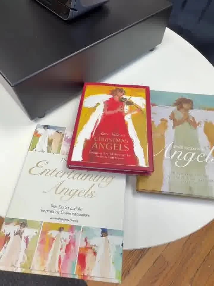 A book titled 'Encountering Angels' with a cover image of an angel and a woman in a red dress, a smaller booklet with a similar theme, and a deck of cards featuring angel imagery on a table near a black electronic device.
