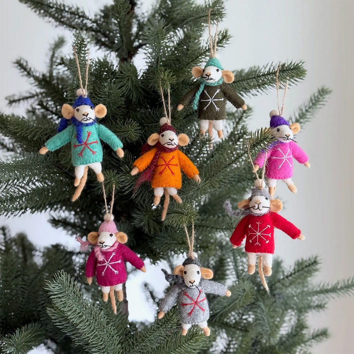 Colorful mouse plush ornaments wearing sweaters and hats hanging on a Christmas tree.