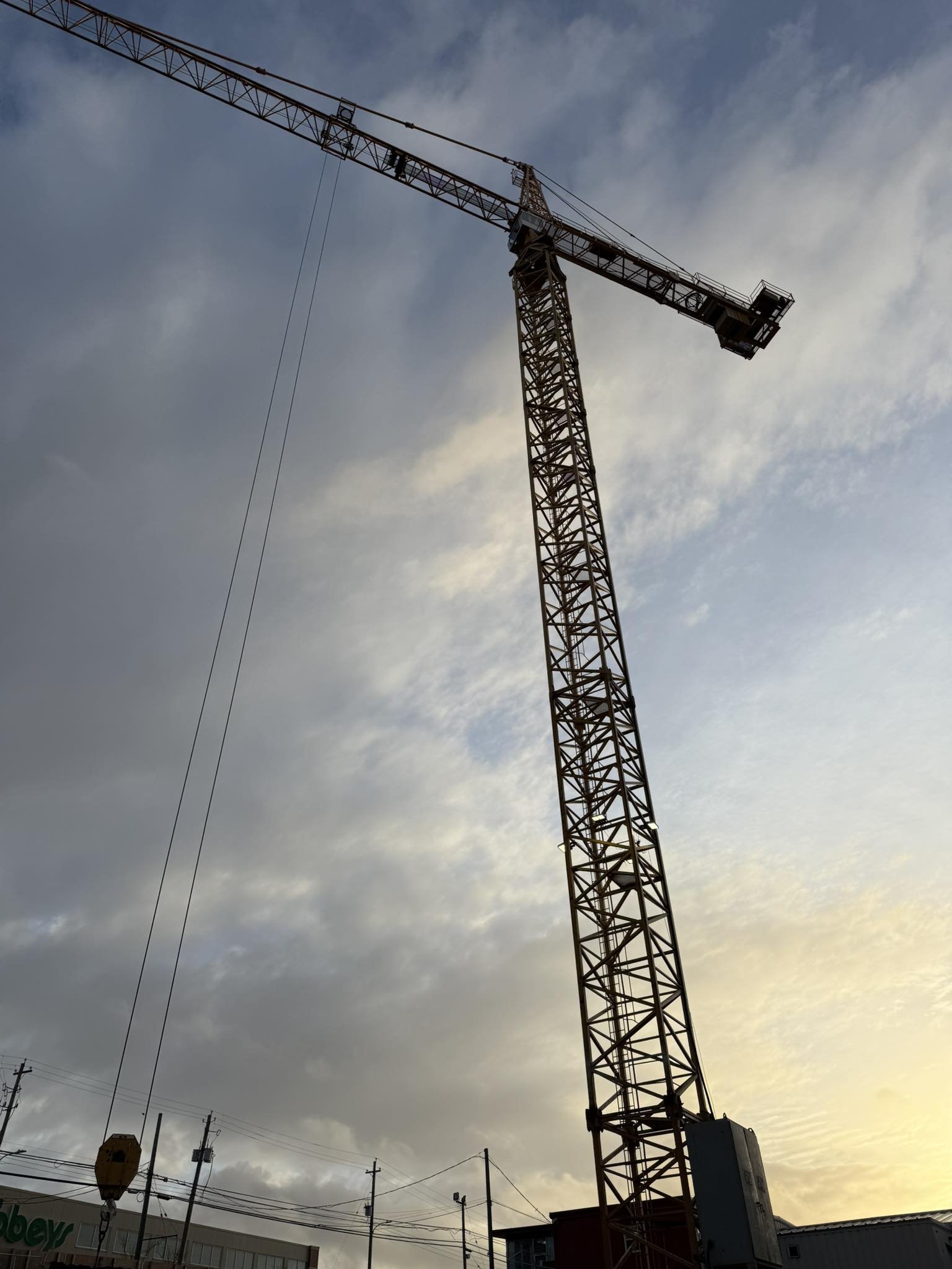 A tall construction crane against a cloudy sky at dusk.