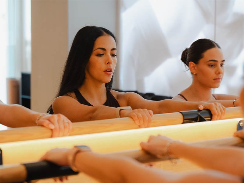 Dos mujeres en una clase de ejercicio, sujetando un barra horizontal con las manos,