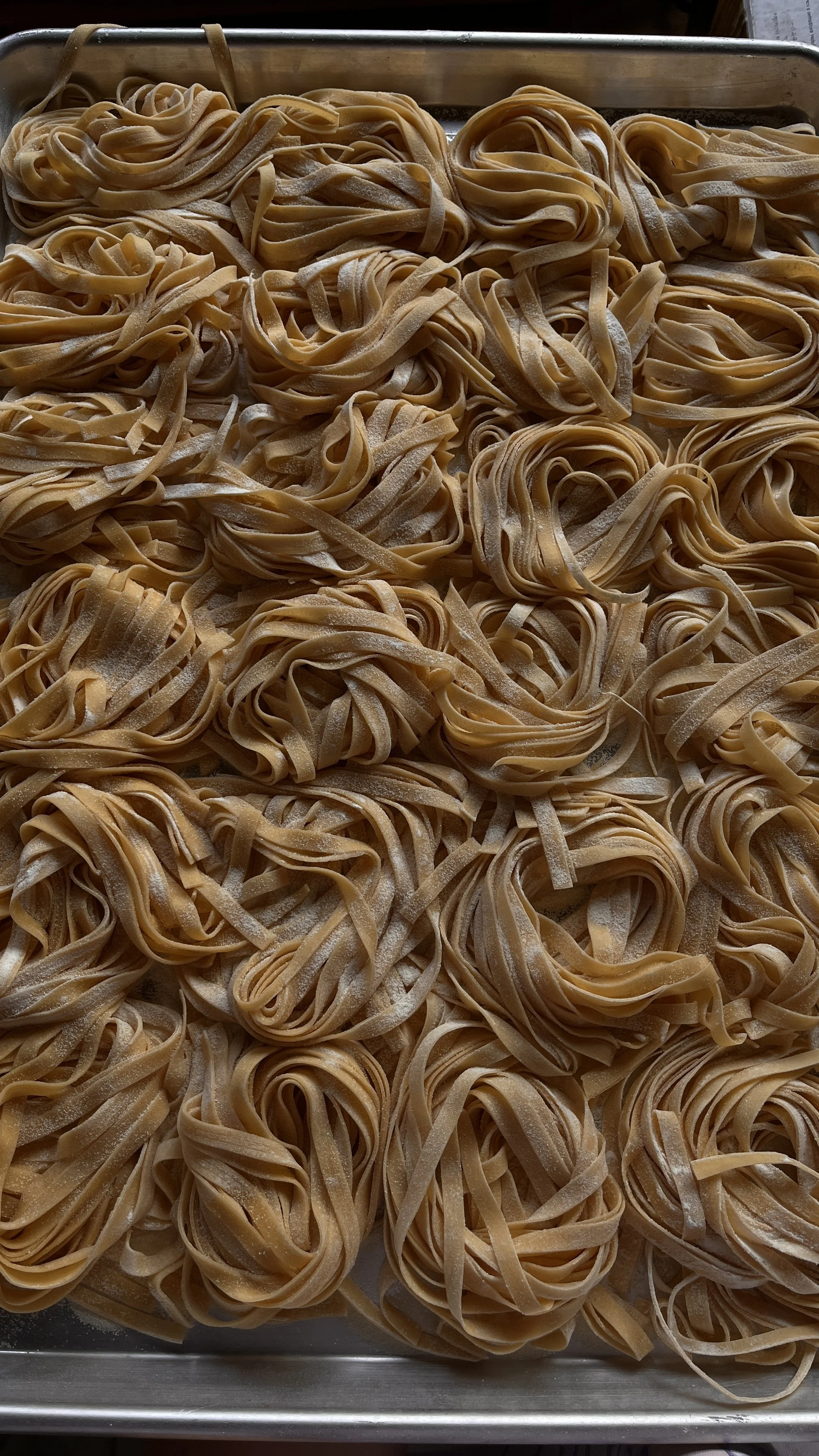 Uncooked fettuccine pasta nests spread out on a baking sheet.