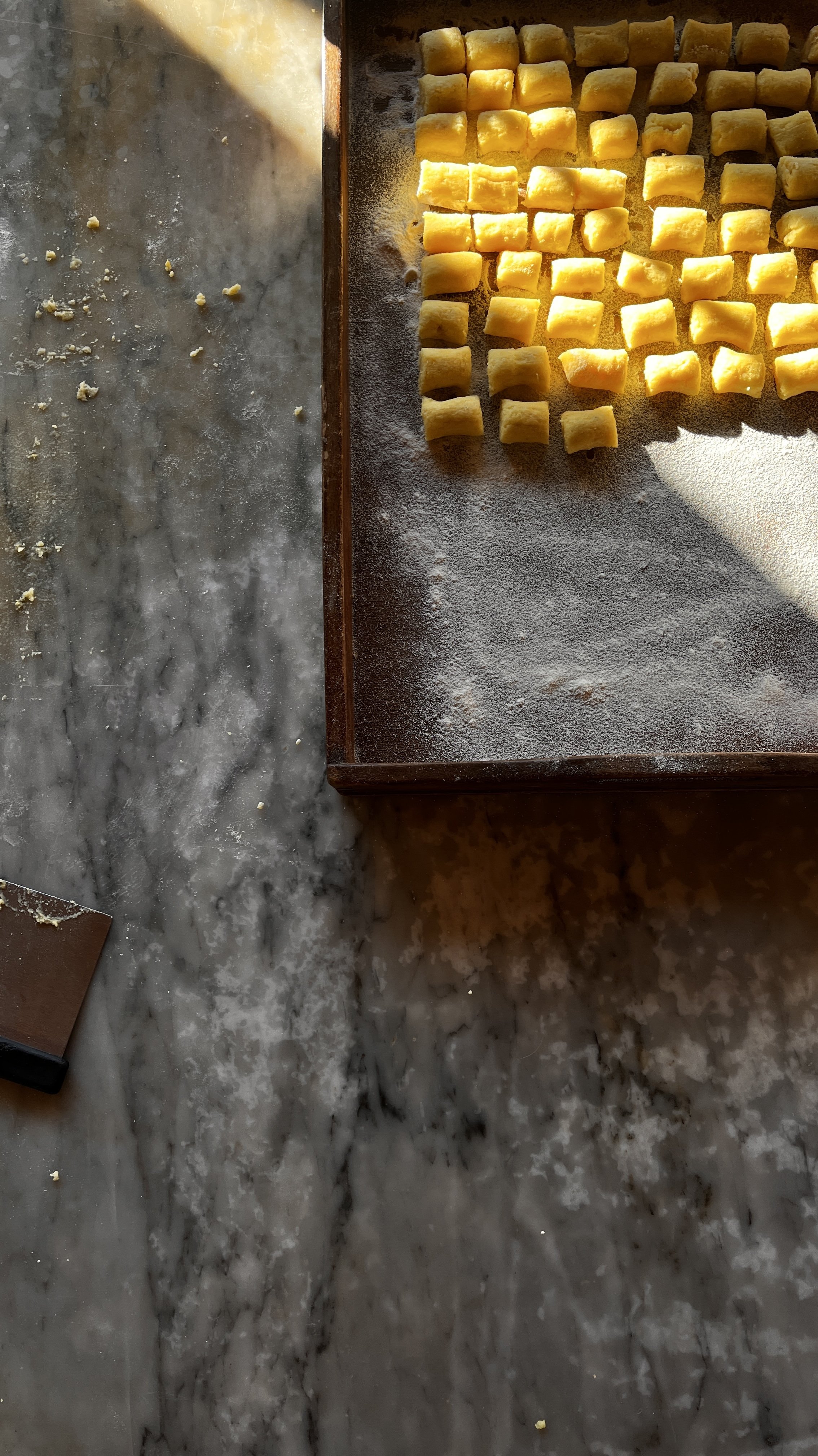 Unmarbled gray and white marble surface with a wooden cutting board holding small yellow dough pieces, some scattered on the surface.