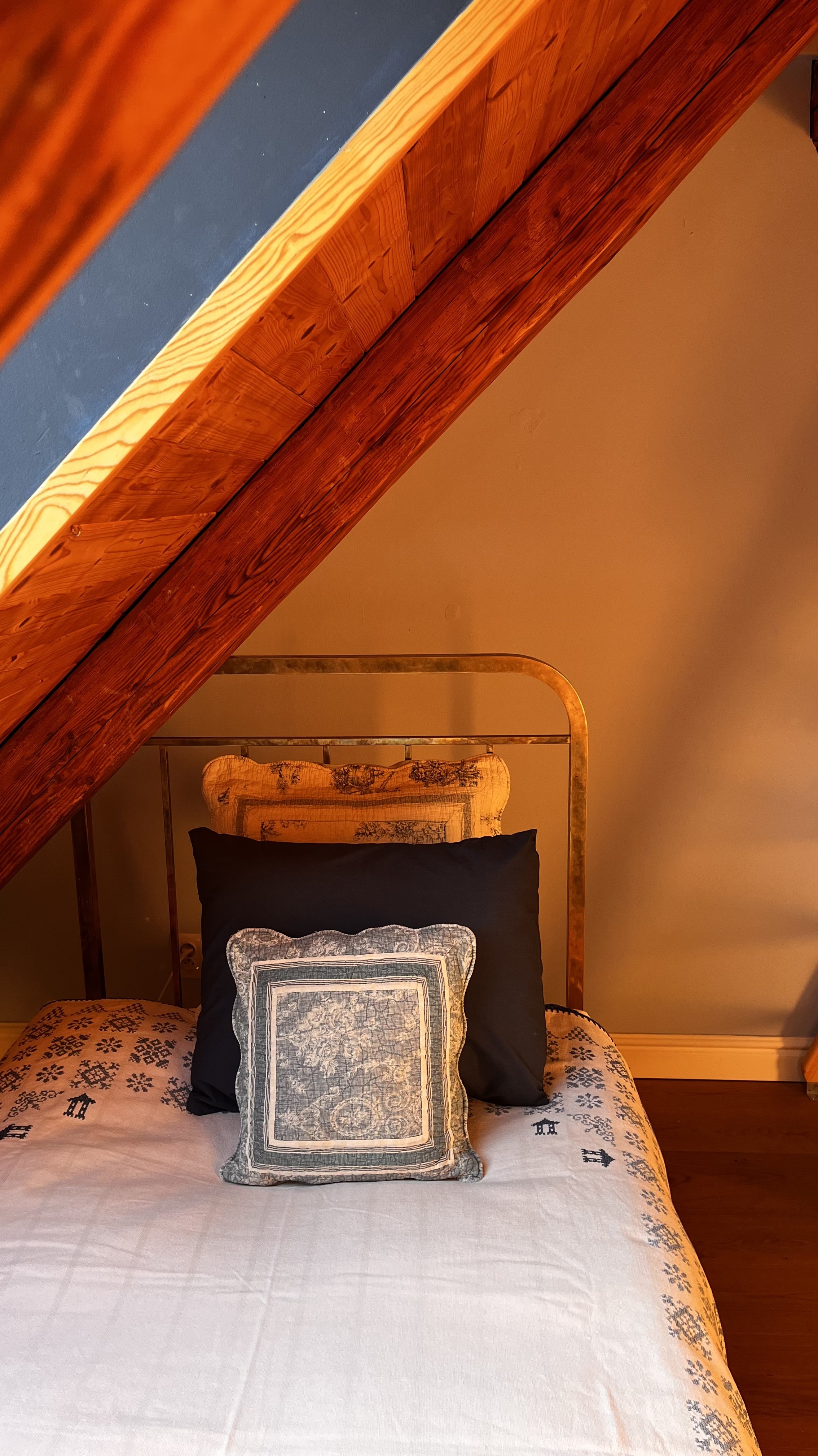 A cozy bed with decorative pillows in a warmly lit room with wooden ceiling beams.