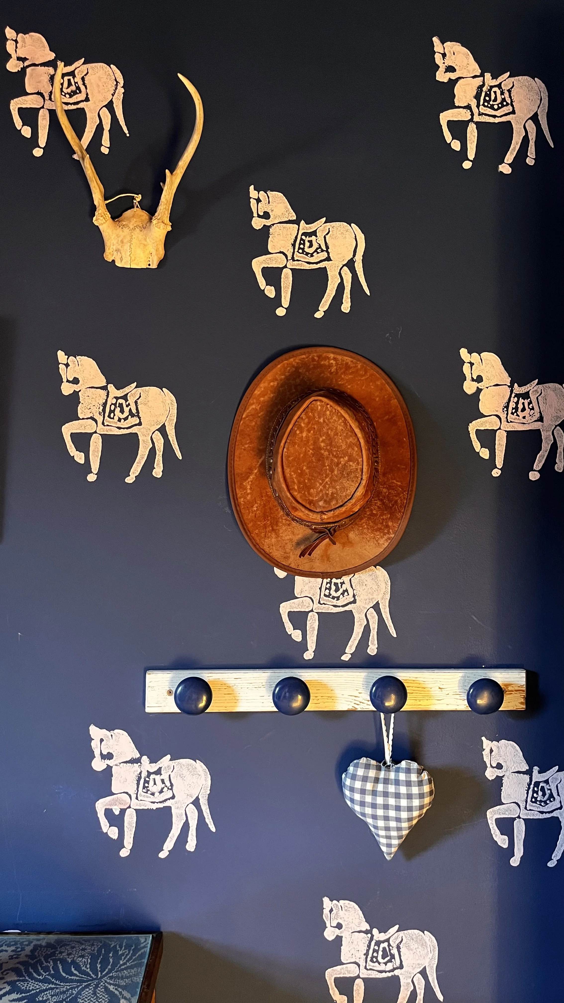 Decorative wall with mounted antler, cowboy hat, and white Christmas gnome, black background with repeated white wolf or dog pattern.