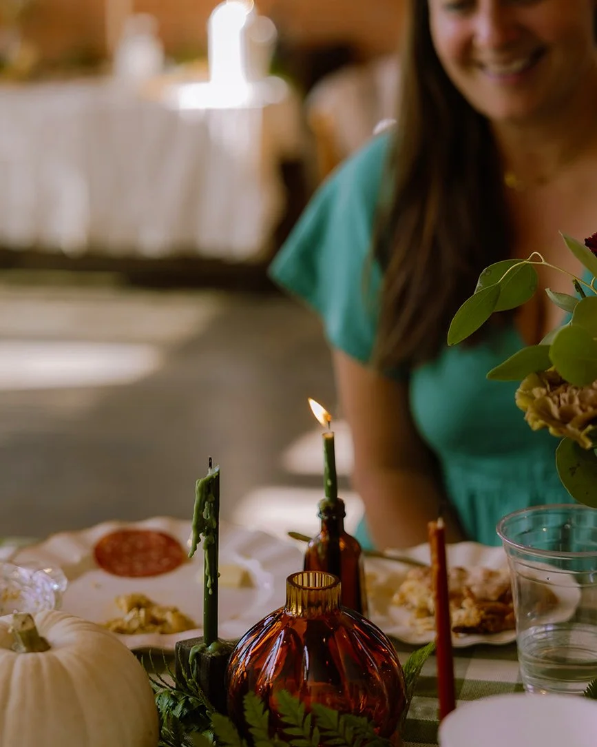 A woman smiling at a table decorated with candles, pumpkins, and flowers during a celebration or meal.