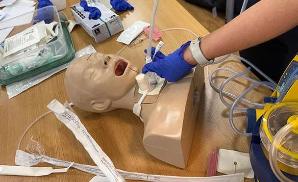 A medical training mannequin being used to practice tracheostomy care and awareness