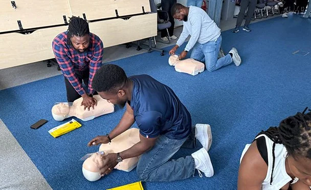 People practicing CPR on mannequins during a training session in a classroom setting.