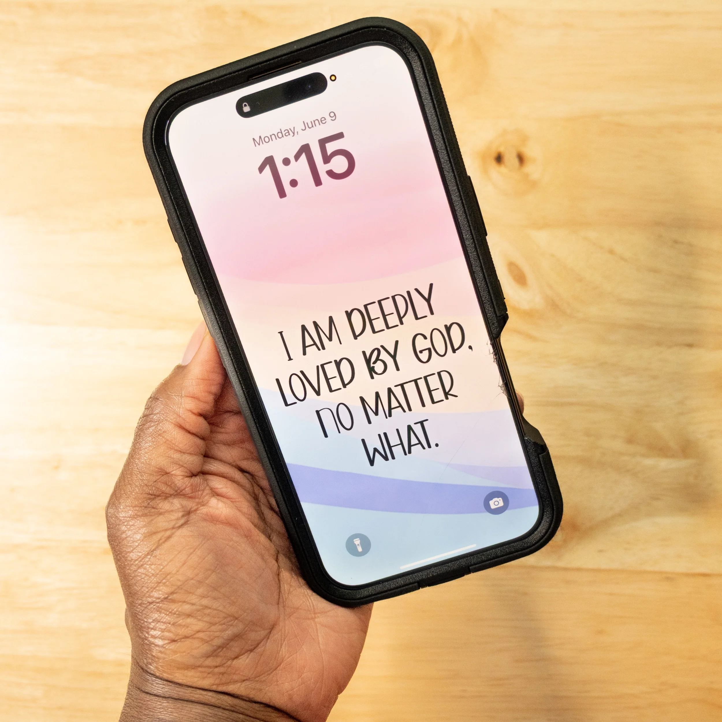 A person holding an iPhone with a message app open displaying the text 'I am deeply loved by GOP, no matter what.' The phone is in a black case and is held over a wooden surface.