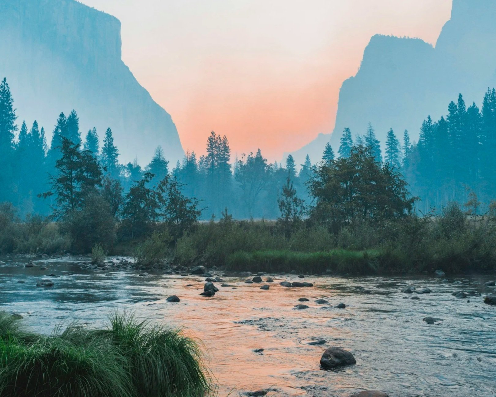 A serene river flowing through a lush valley surrounded by tall trees and mountains, with a pastel-colored sky at dusk.