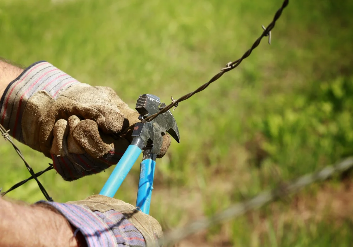 person wearing gloves and using a tool to remove a bared wire fence.